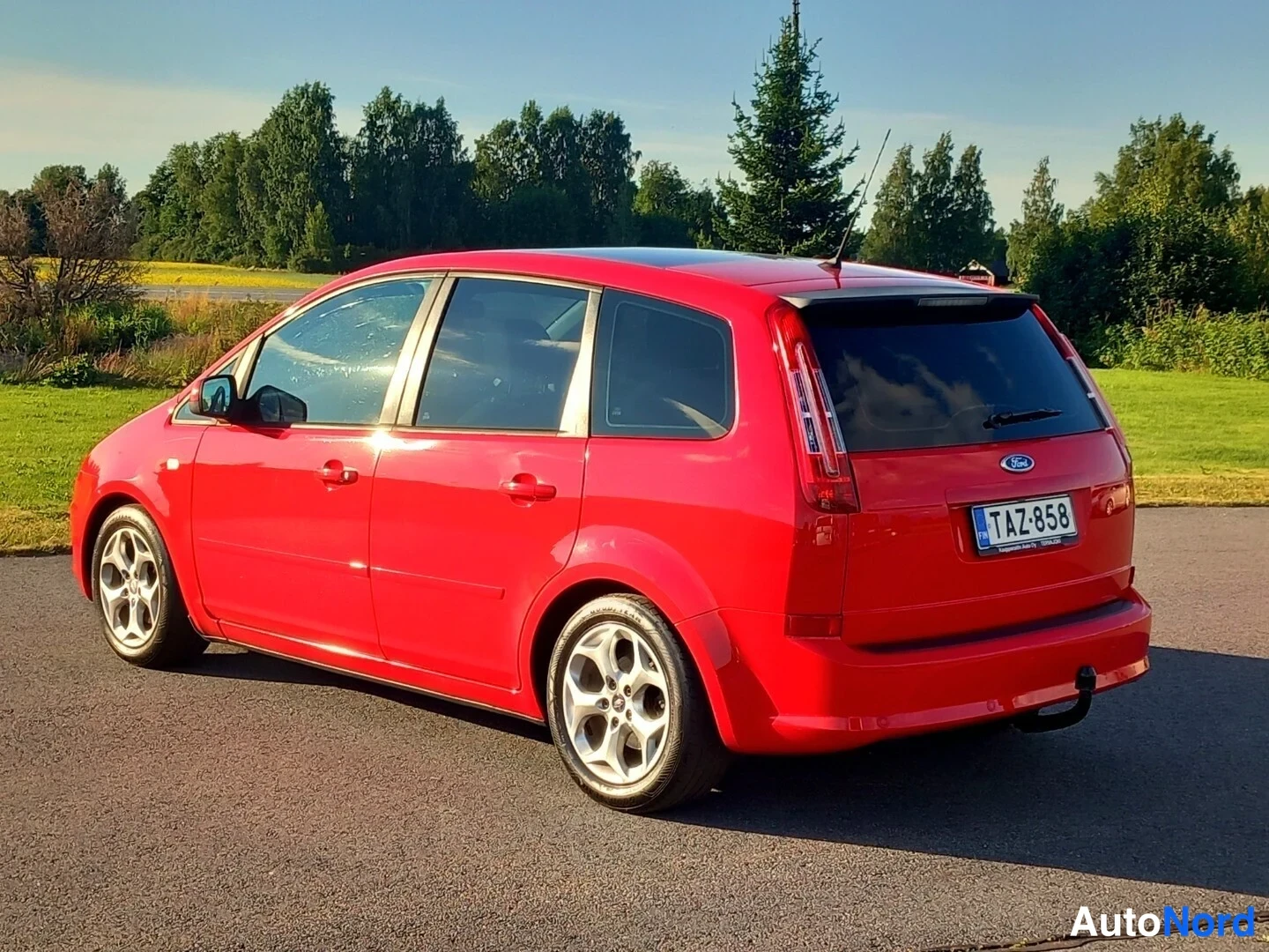 Takaviisto: Punainen tilavautomobiili takaviistosta vasemmalle, takapuhallin ja rekisteritunnus näkyvissä.