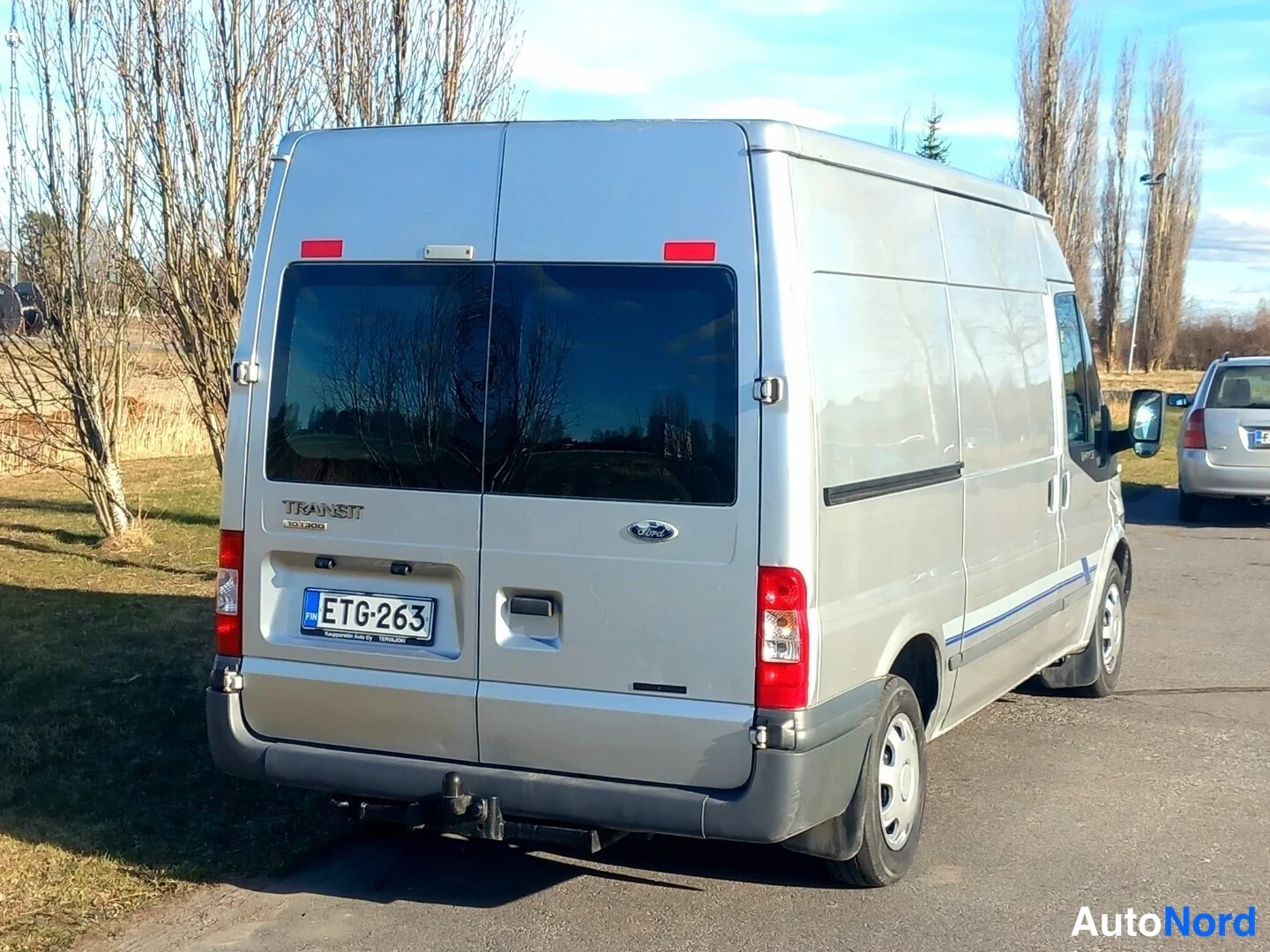 Takaviisto: Ford Transit -pakettiauton takakulma, hopeakarvainen korri ja rekisterikilpi.