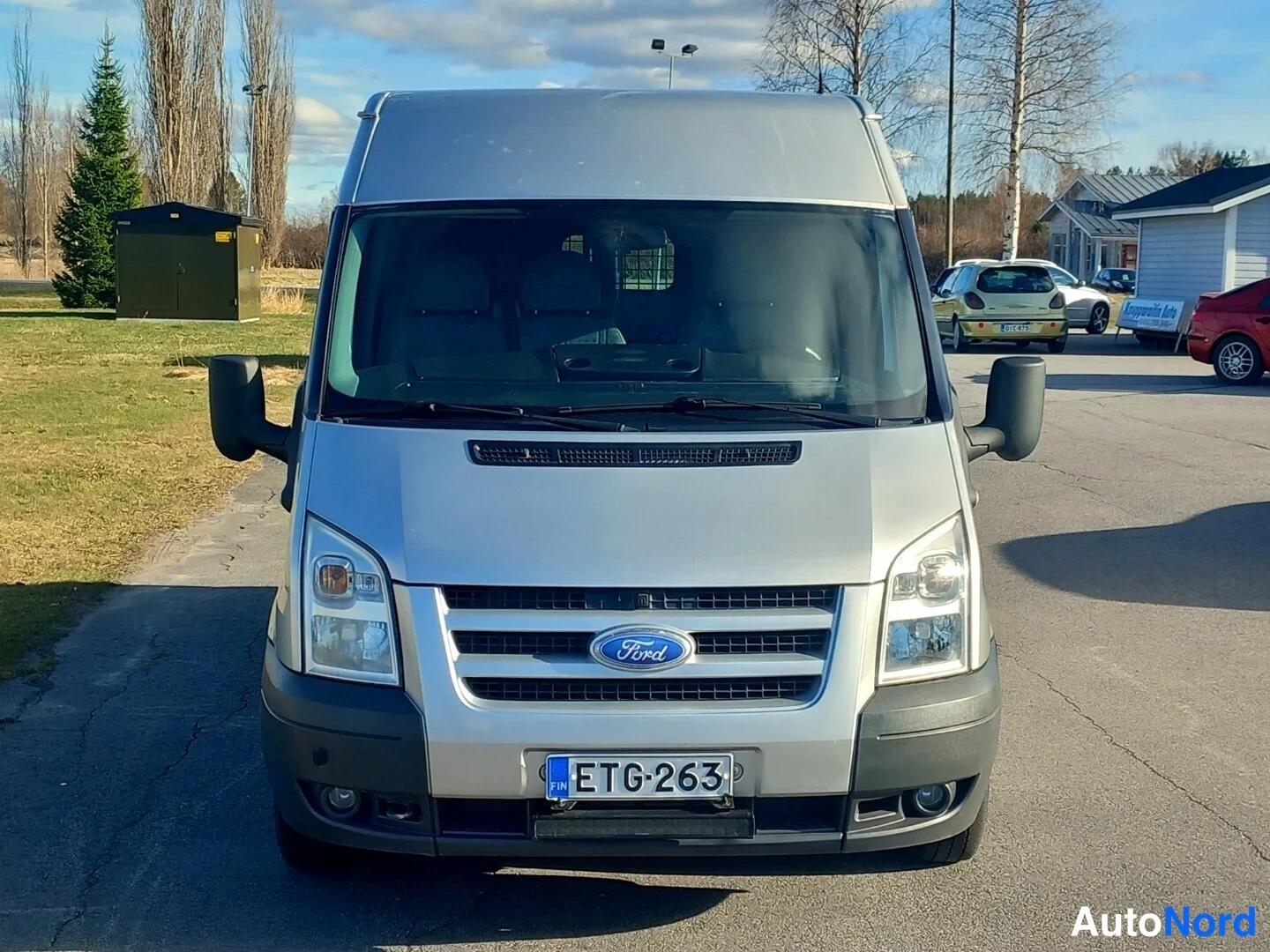 Edestä: Ford Transit -pakettiauto suoraan edestäpäin kuvattuna, Ford-merkki keskellä etusäleikköä, rekisterikilpi.