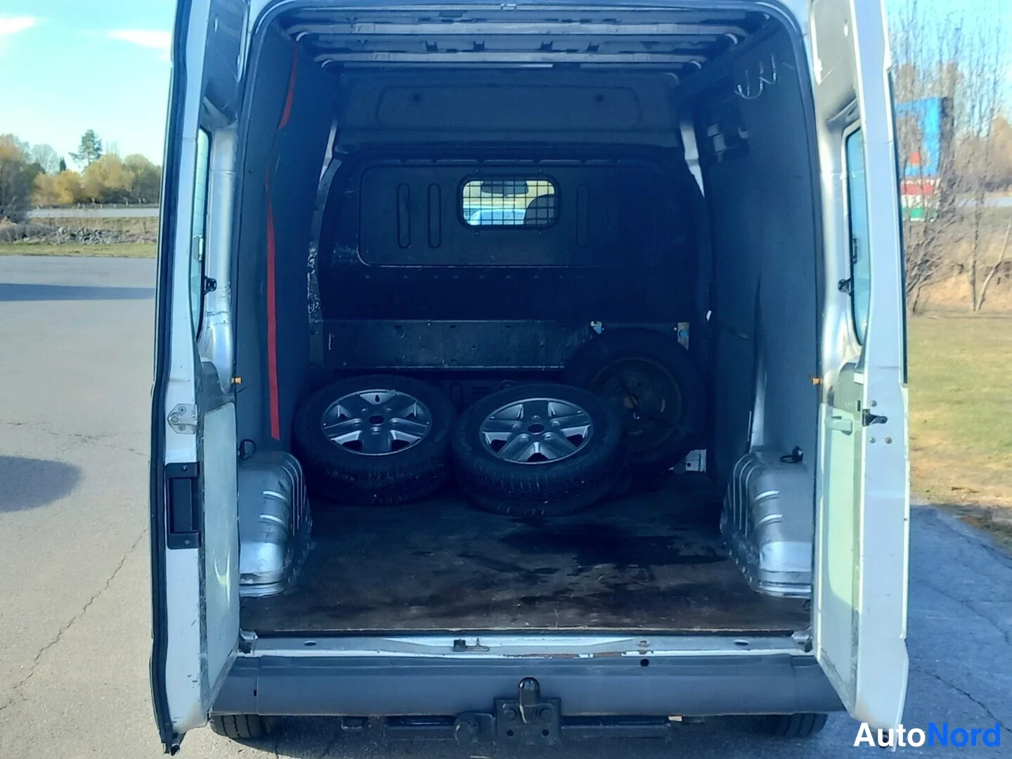 Sivulta: Ford Transit -pakettiauton takaovet auki, tyhjä lastaustila, lattialla neljä pyörää ja irrotettu varaosa.