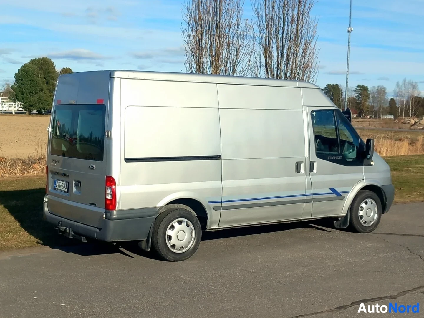 Takaviisto: Ford Transit -pakettiauto hopeanvärisenä takaa kolmesta neljäsosasta, takavalot ja rekisterikilpi näkyvissä.
