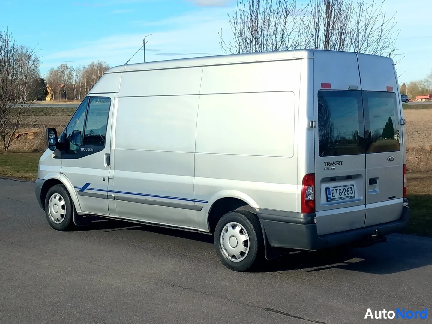 Takaviisto: Hopeanvärinen pakettiauto kuvattu takaa-vinosti, rekisterikilpi, sivussa sininen koristelista.