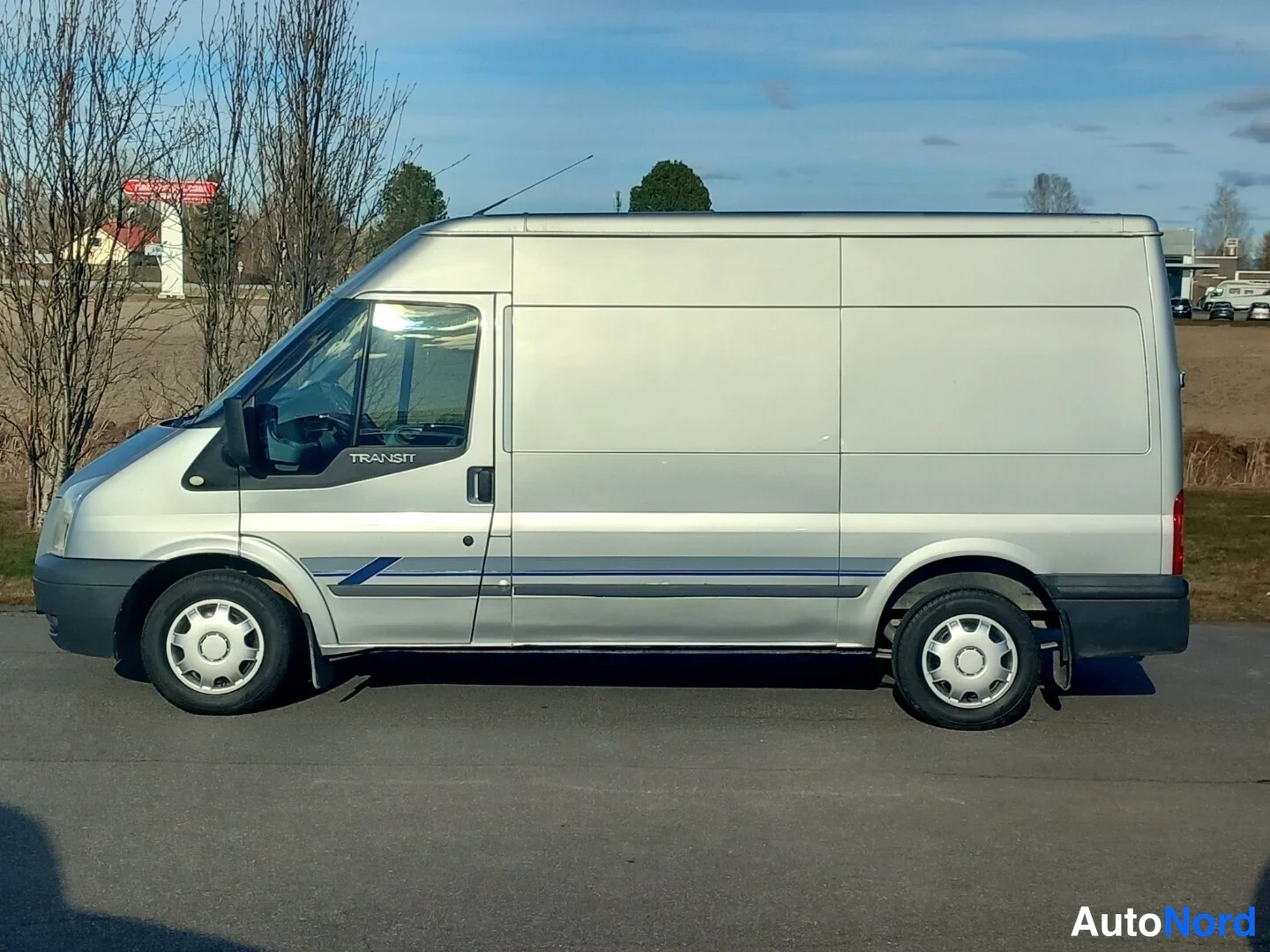 Sivulta: Hopeanvärinen pakettiauto sivulta vasemmalta, TR-kylkiteksti ja sininen koristelista näkyvissä.