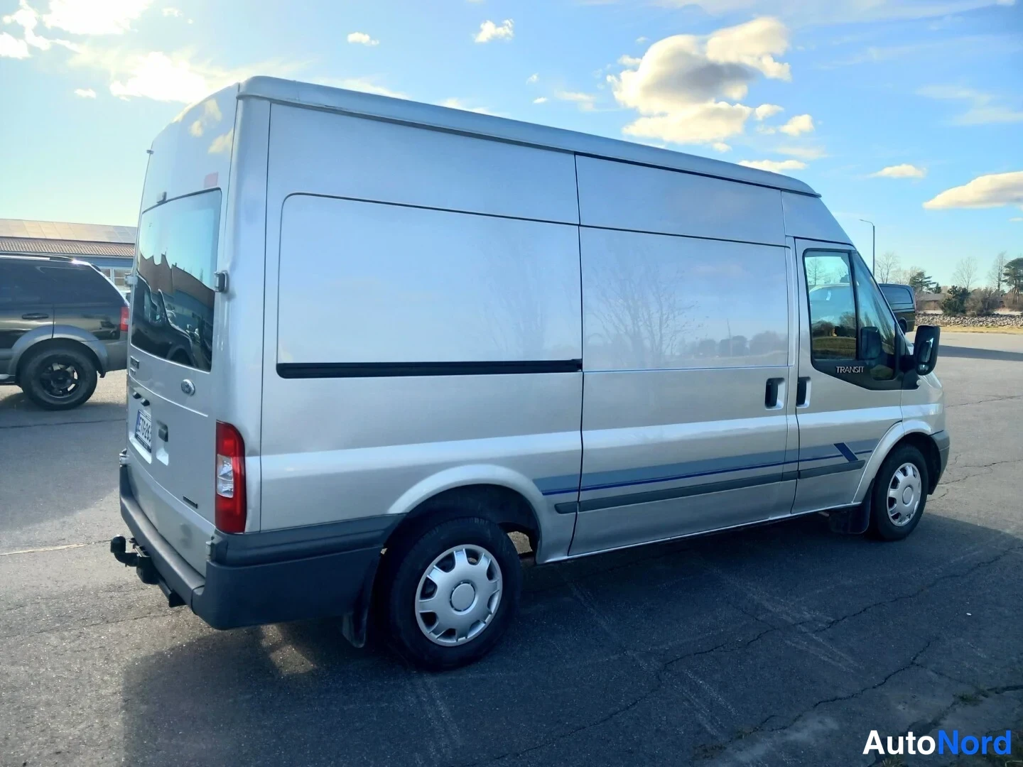 Takaviisto: Hopeanharmaa Ford Transit -pakettiauto kuvattu takaviistosta, takaovi ja kylki näkyvät.