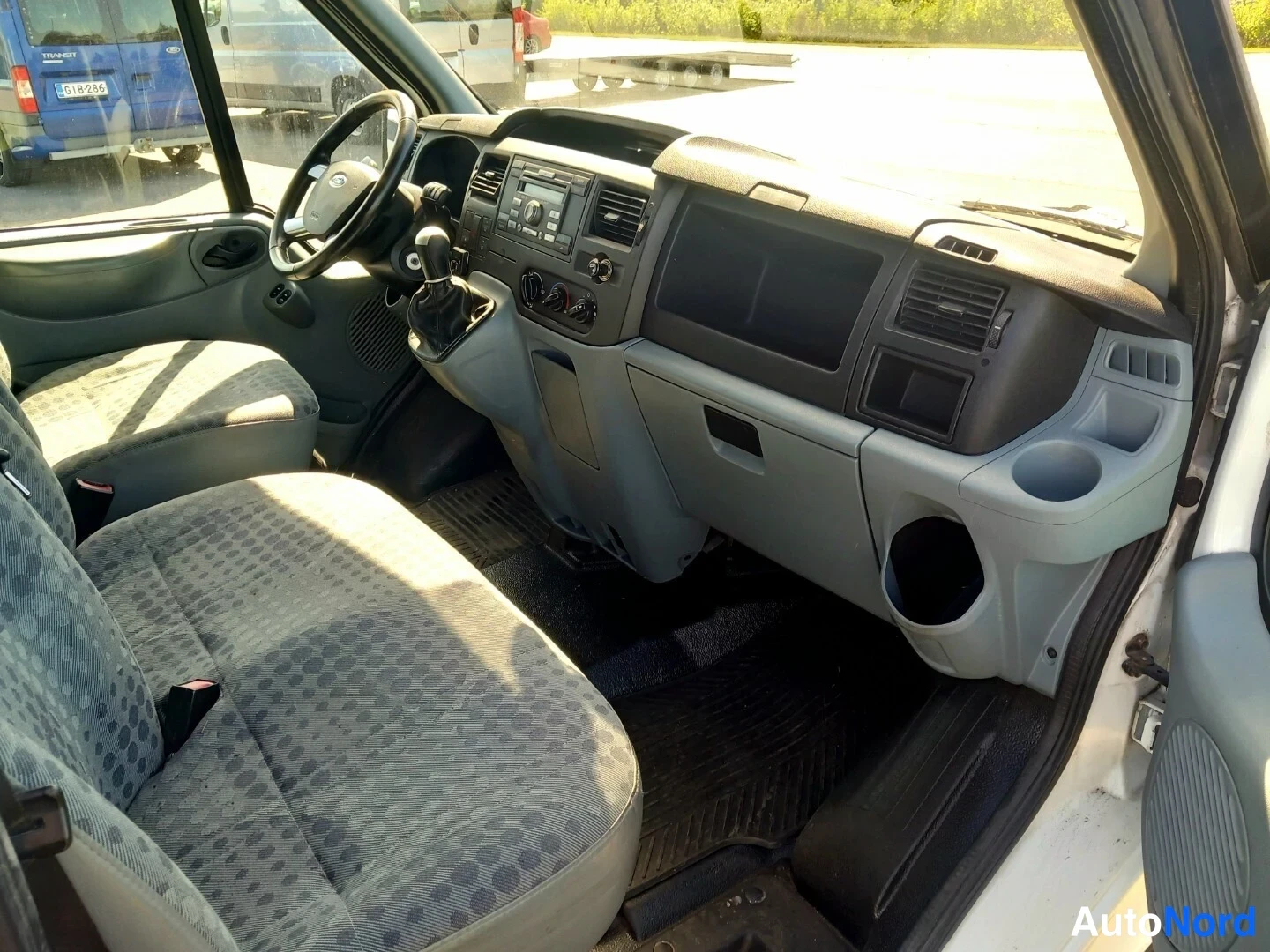 Muu: Kuljettajan ja matkustajan istuimet, ohjauspyörä, käsivaihteisto ja kojelauta radioineen Ford Transitin sisätiloissa.
