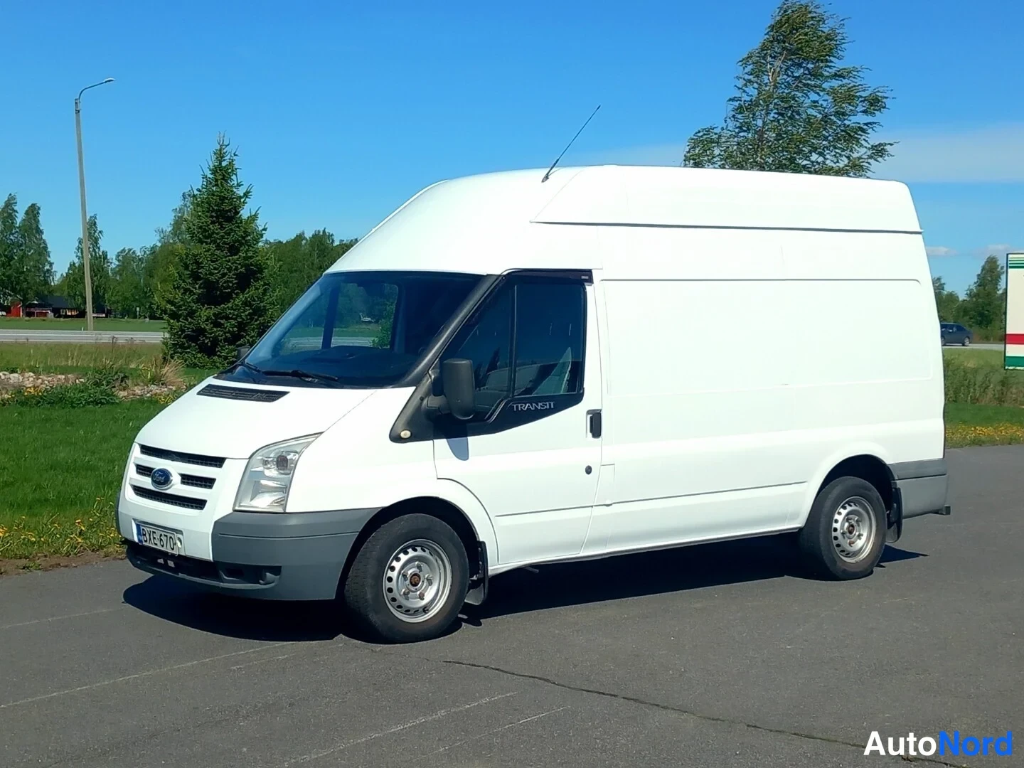 Etuviisto, nokka vasemmalle: Valkoinen Ford Transit -pakettiauto kulmaotoksessa, keula vasemmalla