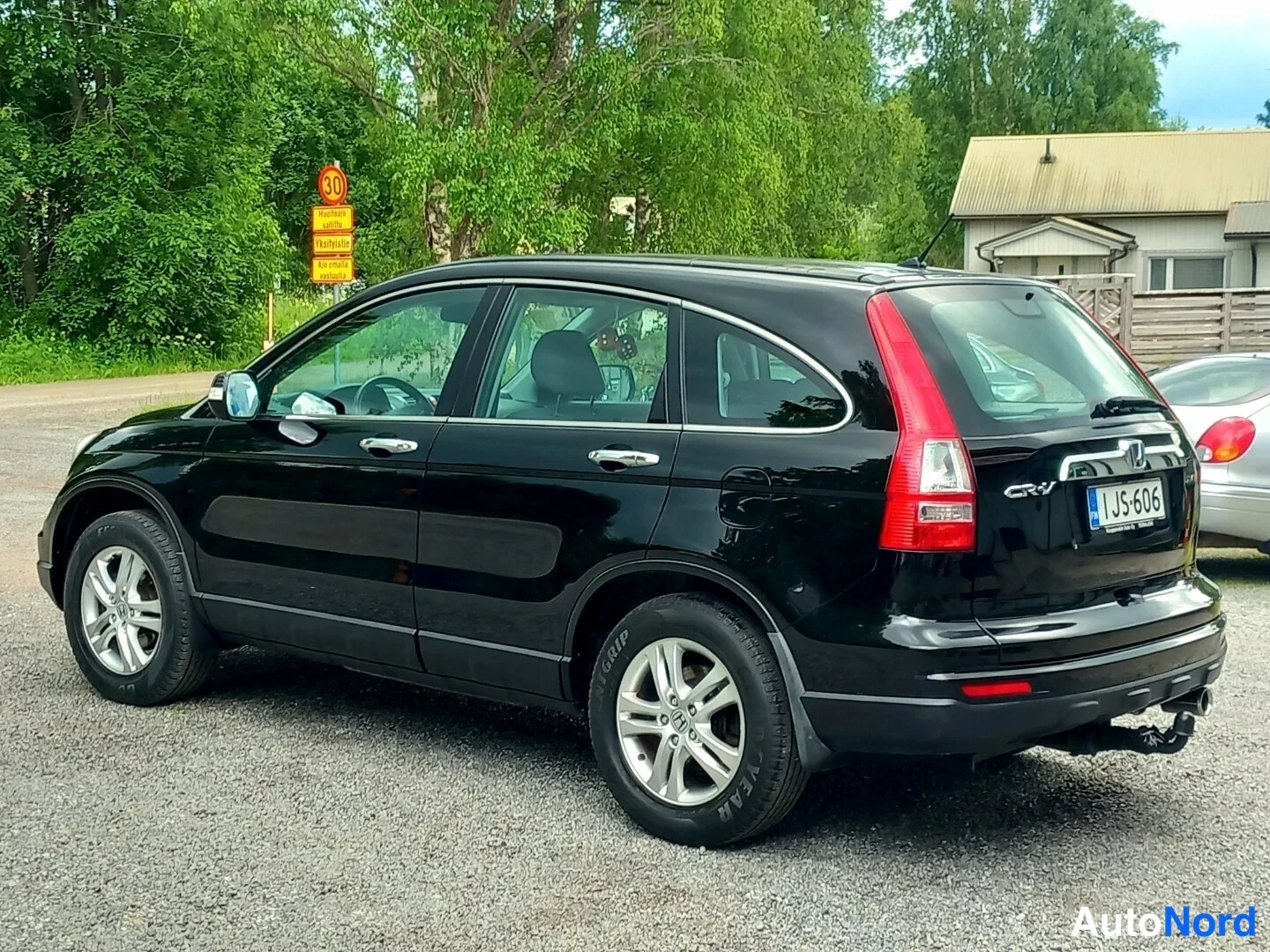 Takaviisto: Musta Honda CR-V kolmeen neljäsosaan takaa vasemmalta nähtynä, rekisterikilpi, vetokoulu ja hopeavanteet näkyvät.