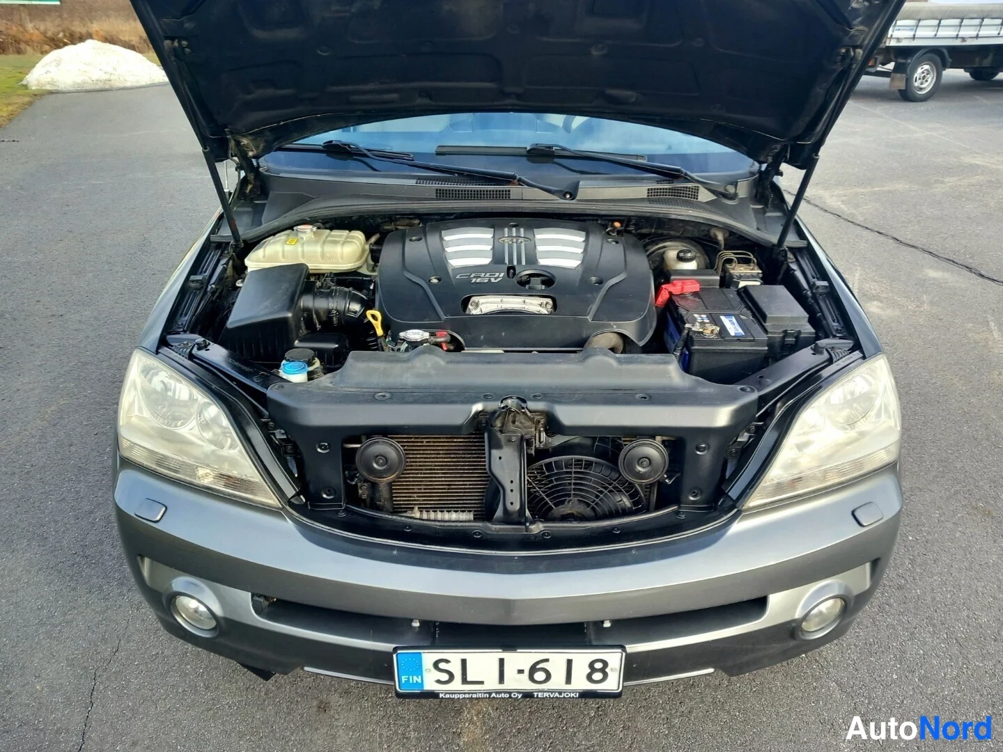Edestä: Kia Sorenton konepelti auki etukäteen kuvattuna; dieselmoottorin suojus, akku oikealla, lauhde- ja jäähdytyspallo näkyvät, rekisterikilpi.