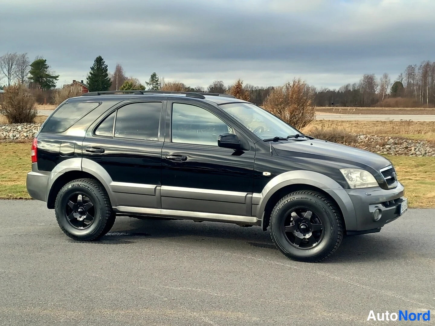 Etuviisto, nokka oikealle: Musta Kia Sorento -suv etu- ja sivukulmassa, mustat vanteet, kattokaaret.