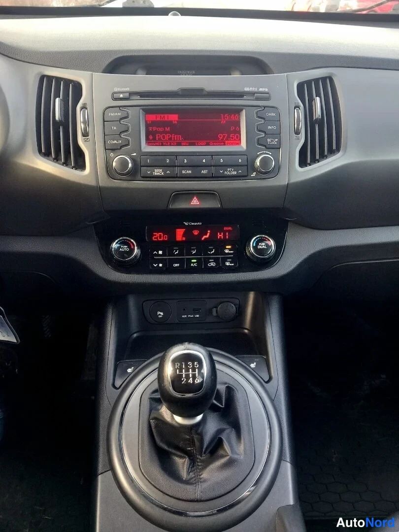Muu: Keskikonsolin lähikuva: radio näytöllä radioasema 97.50, automaattinen ilmastointi (A/C, AUTO) ja manuaalivaihteen keila.