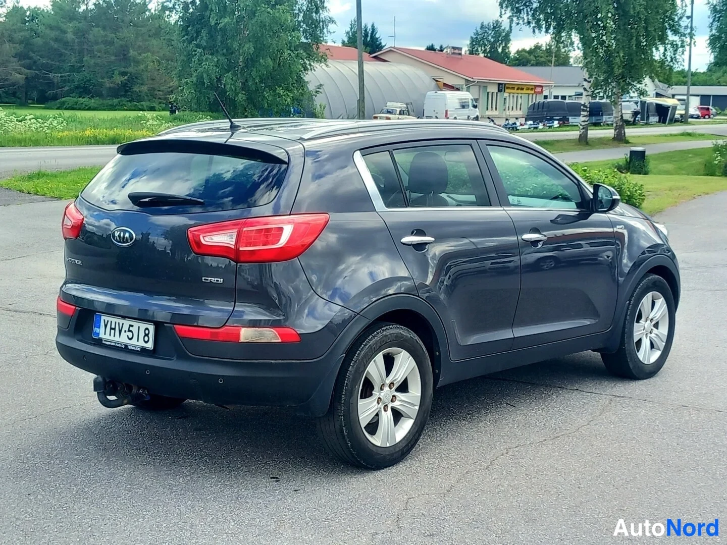 Takaviisto: Tummanharmaa Kia Sportage takakulmasta; näkyvät takavalot, takaluukki, vasen kylki, vetokoukku ja rekisterikilpi.