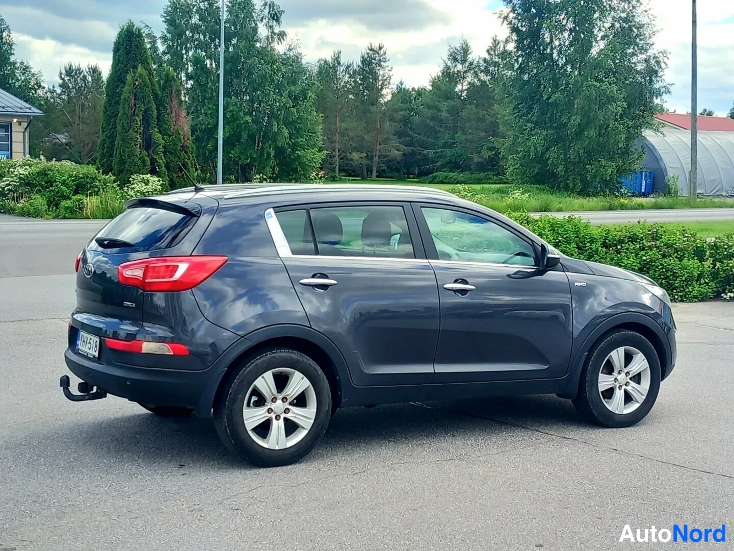 Takaviisto: Sinertävän harmaa Kia Sportage -maastopotkuri sivulta takaa vasemmasta kulmasta kuvattuna; takavalot, tavaratilan luukku ja vasen kylki näkyvissä, lukkiutumatto