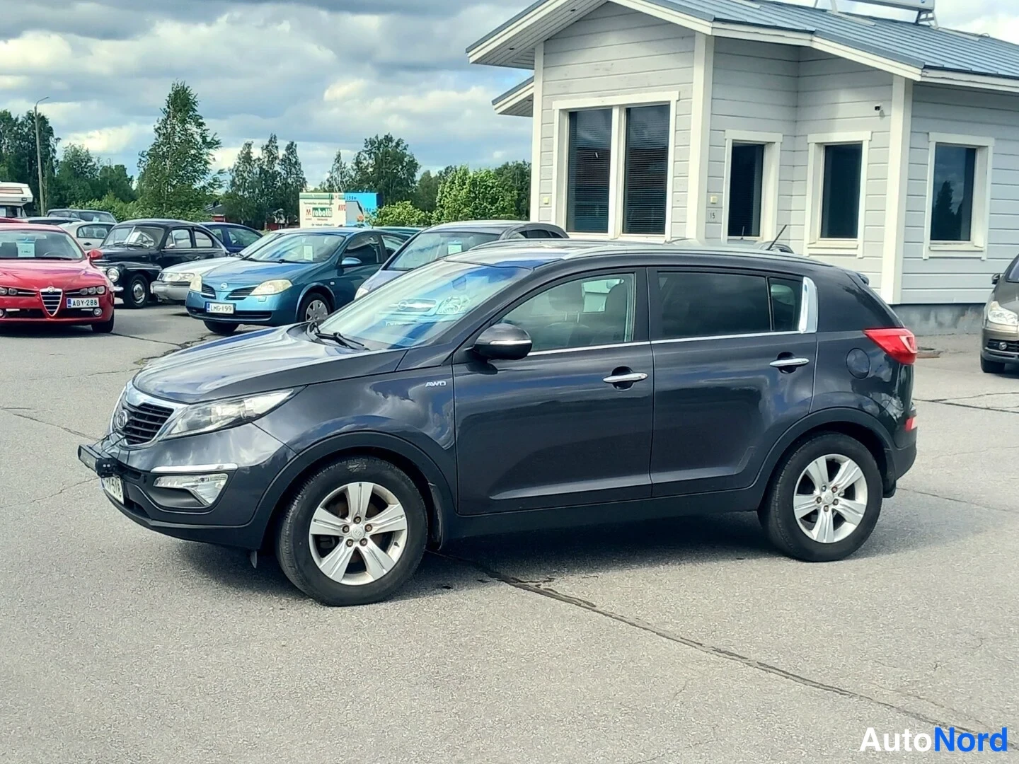 Etuviisto: Kia Sportage edessä vasemmasta kulmasta; etusäleikkö ja ajovalot sekä vasen kylki näkyvissä, peltikori merkinnätön.