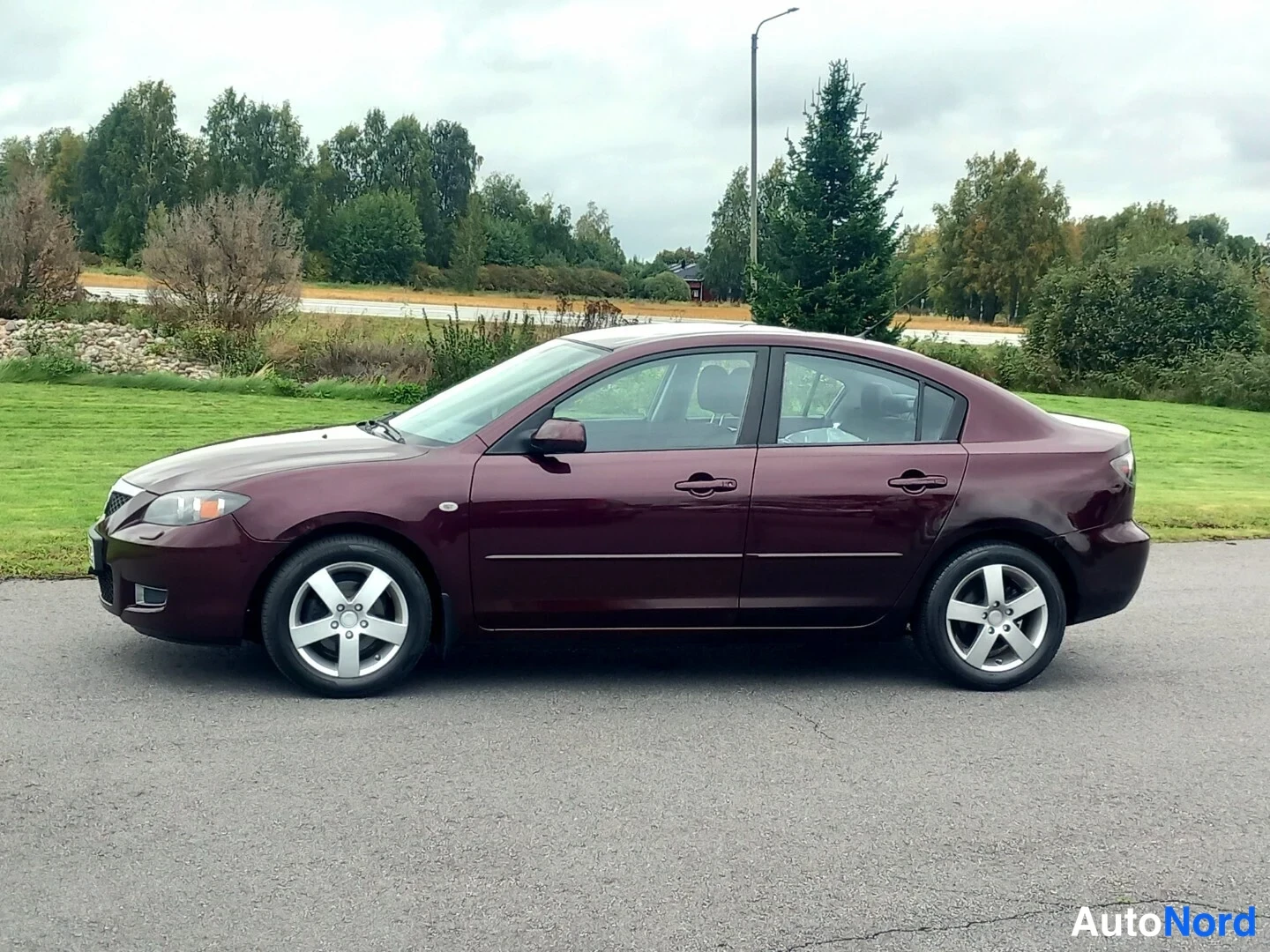 Etuviisto: Tummanpunaisen Mazda 3 -sedanin etusivu vasemmalta valokuvattuna