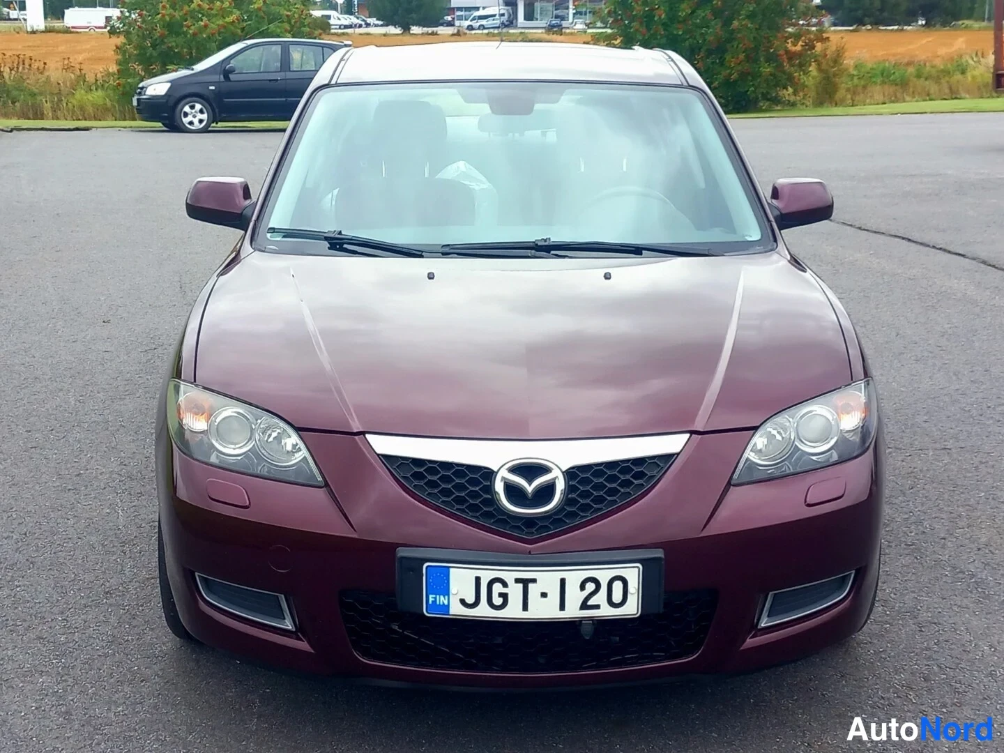 Edestä: Tummanpunaisen Mazda 3 -sedanin etupää; rekisterikilpi lukee