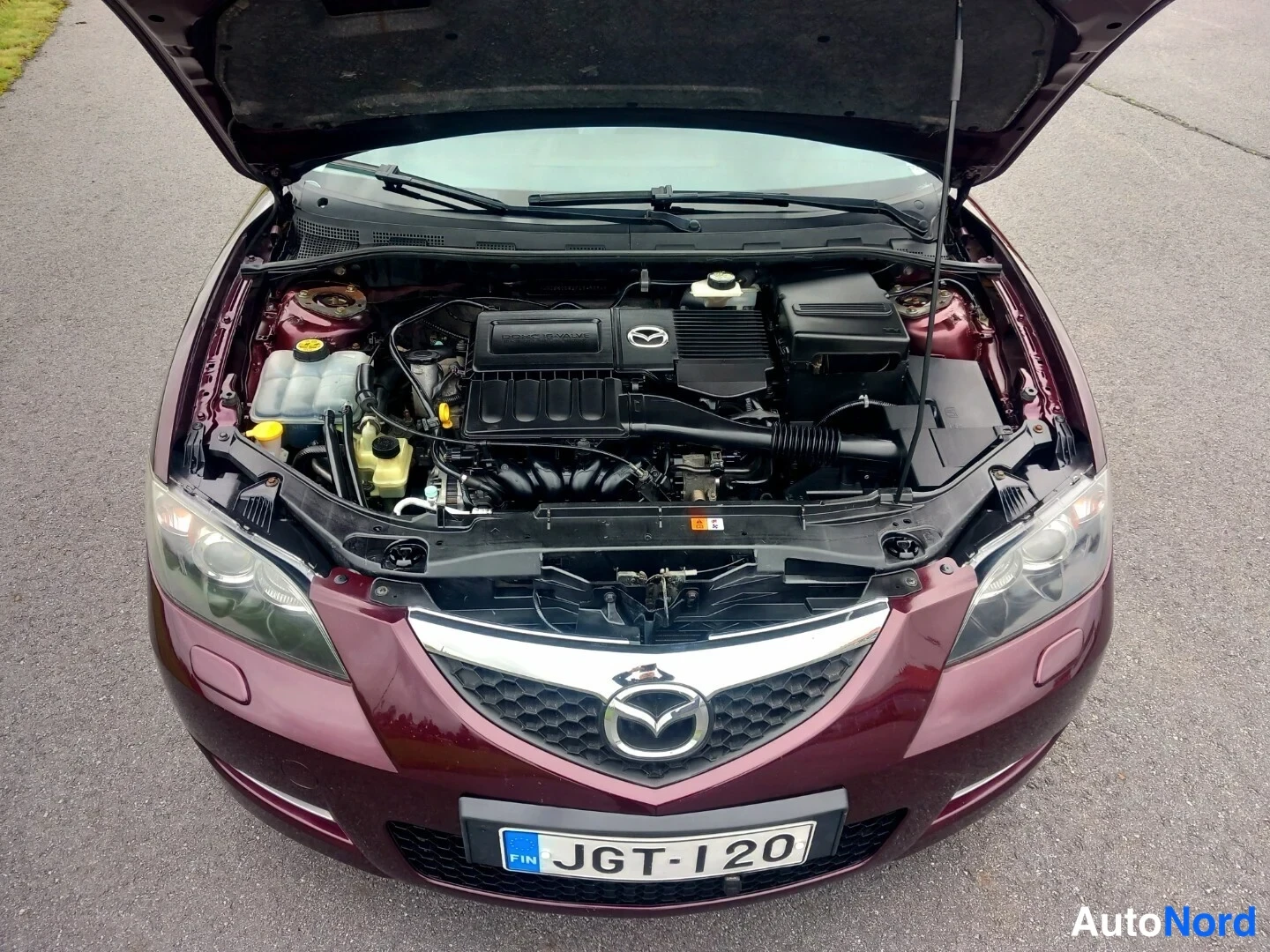 Muu: Tummanpunaisen Mazda 3 -sedanin avoin moottoritila; rekisterikilpi