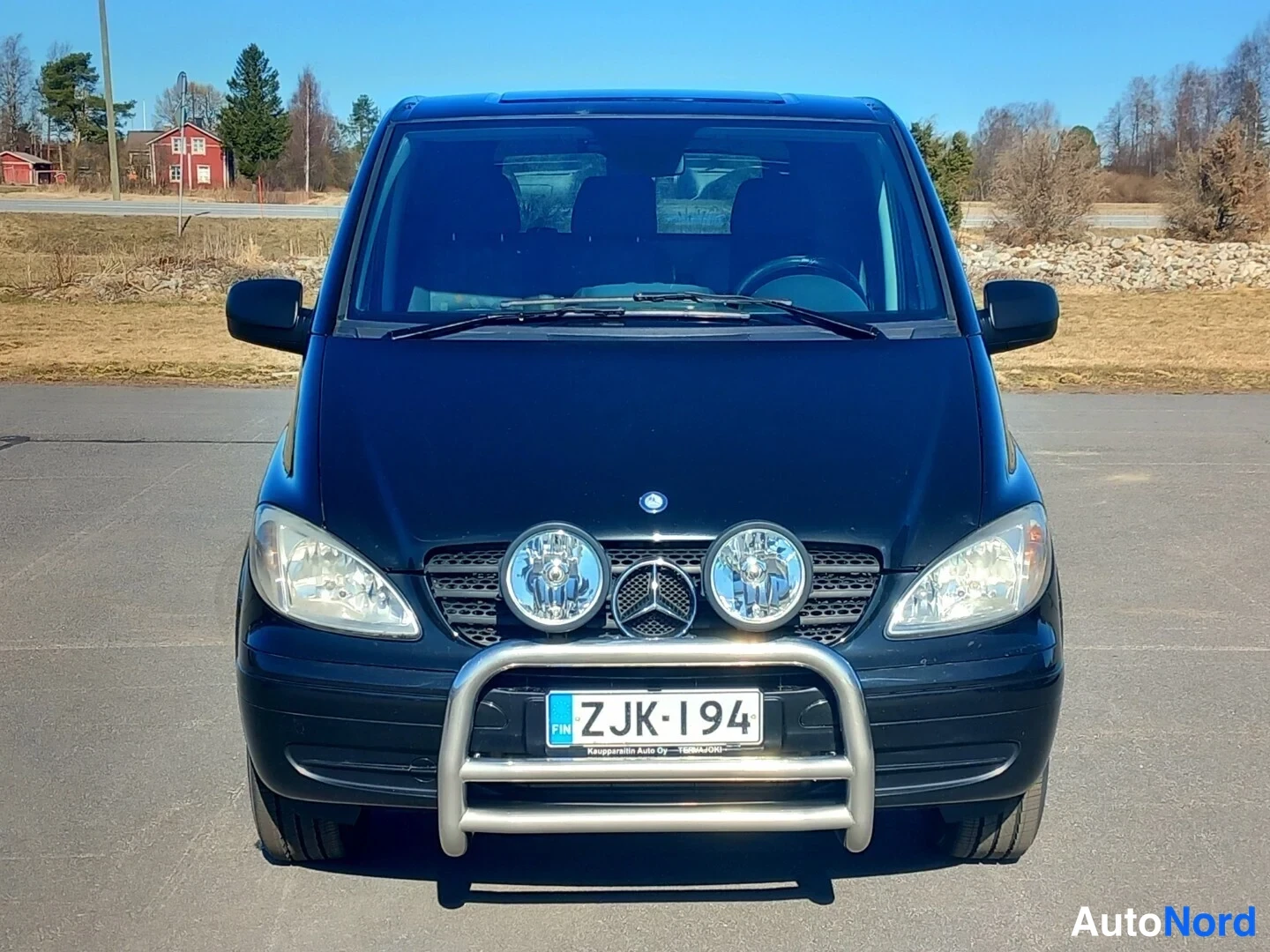 Edestä: Mustan Mercedes-Benz Vito -pakettiauton etunäkymä, kaksi lisävaloa ja Mercedes-tähti maskissa, suojakaari puskurissa, rekisterikilpi.
