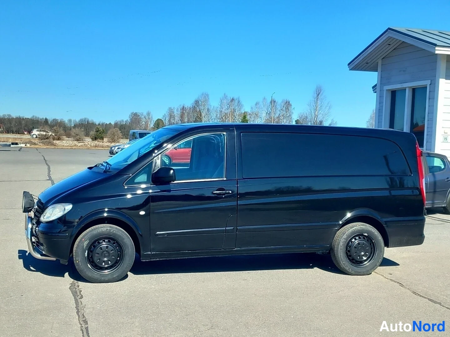 Etuviisto, nokka vasemmalle: Musta Mercedes-Benz Vito -pakettiauto neljännes etusivukulmassa, keulakaari ja tummat peltipyörät näkyvät.