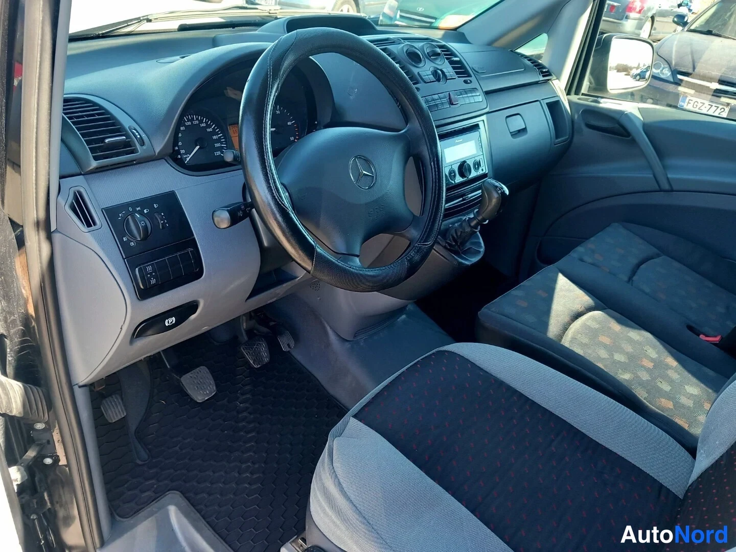 Muu: Mercedes-Benz Vito -henkilöauton ohjaamo: ratin, mittariston ja manuaalivaihtoehdin näkyvä sisätilakuva, mustat kumimatot ja kankaanverhoillut penkit.
