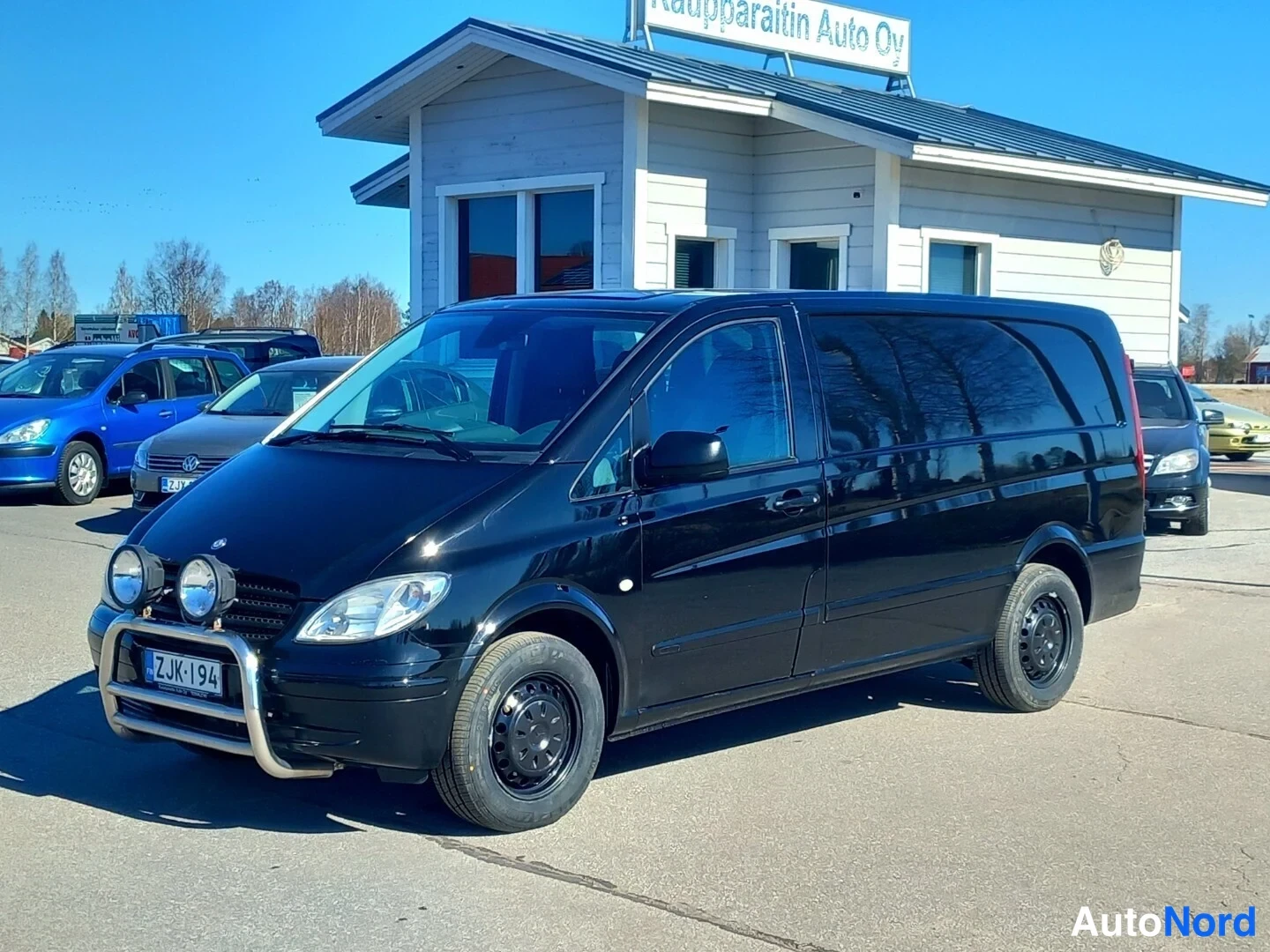 Etuviisto, nokka vasemmalle: Musta Mercedes-Benz Vito -pakettiauto kolmannelta sivusuunnalta, keulavalojalka ja lisävalot