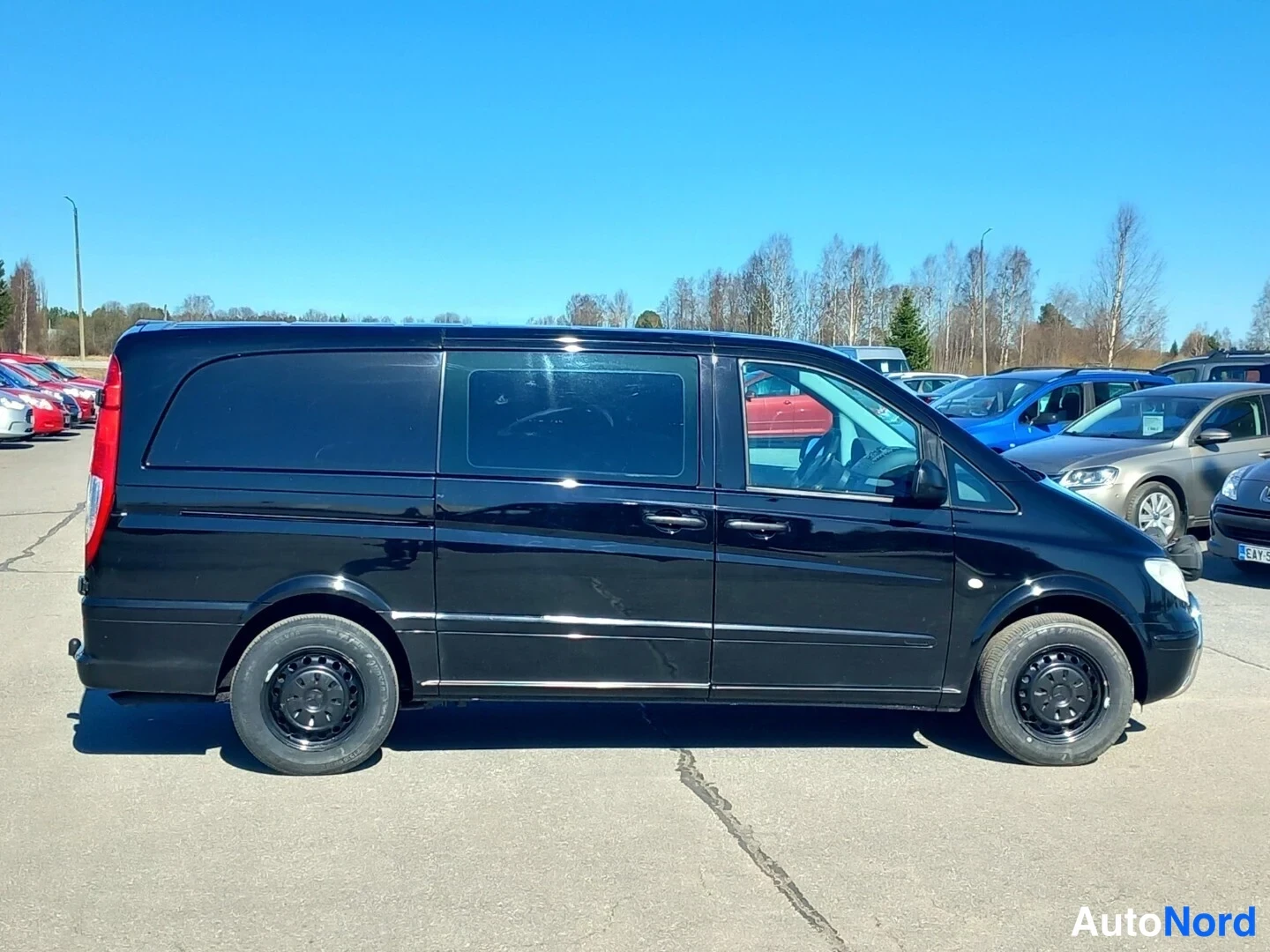 Takaviisto: Mustan Mercedes-Benz Vito -pakettiauton takaosaa ja oikeaa kylkeä, takavalo ja sivuikkunat näkyvät aurinkoisella parkkipaikalla.