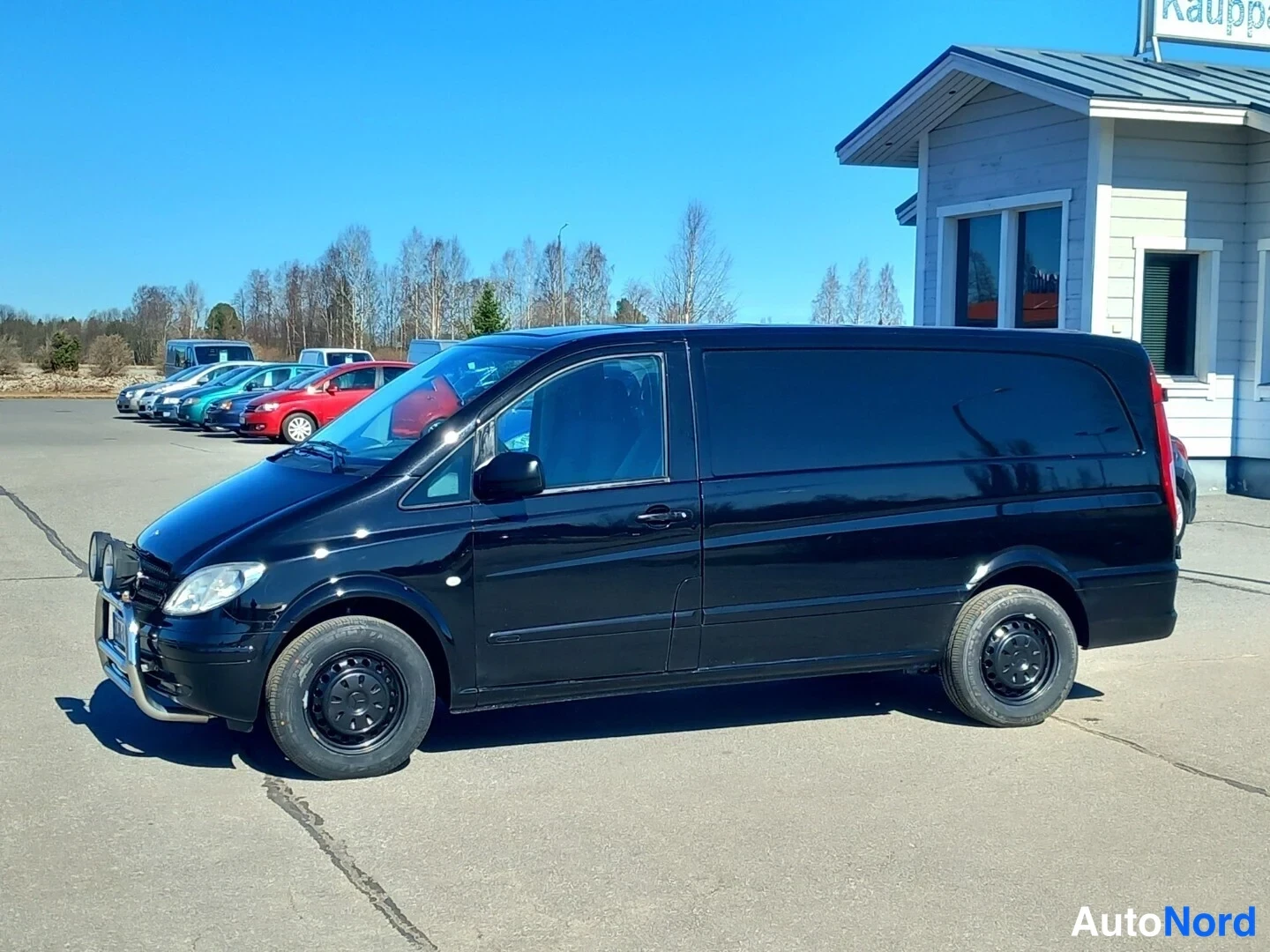 Etuviisto, nokka vasemmalle: Mustan Mercedes-Benz Vito -pakettiauton etuosa ja oikea kylki kolmannelta neljäsosakulmalta, keula vasemmalla, sumvalyhtyrunko etupuskurissa.