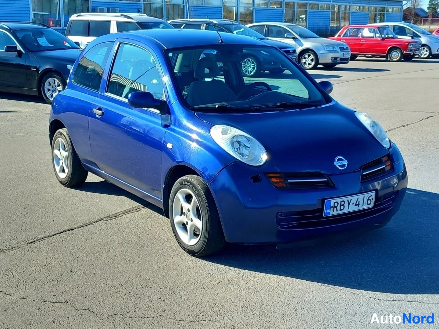 Etuviisto, nokka oikealle: Sininen Nissan Micra edestä vasemmalta kuvattuna, rekisterikilpi.