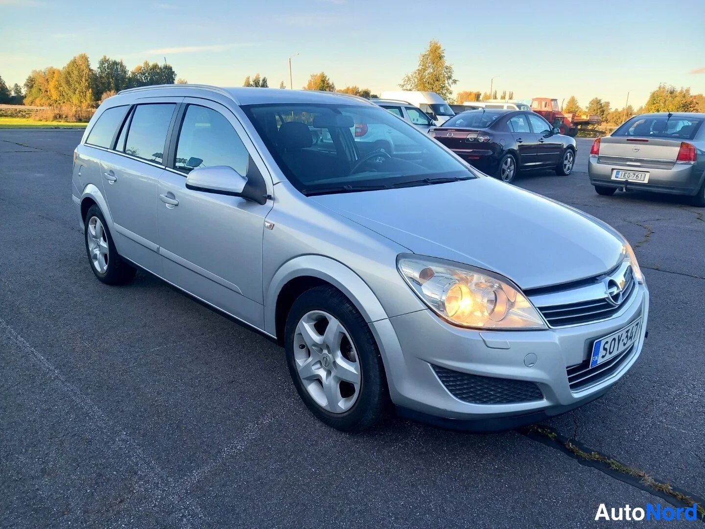 Etuviisto, nokka oikealle: Hopeanvärinen Opel Astra -farmari etuosaltaan oikeasta kolmannesta kuvakulmasta parkkipaikalla, rekisterikilpi.