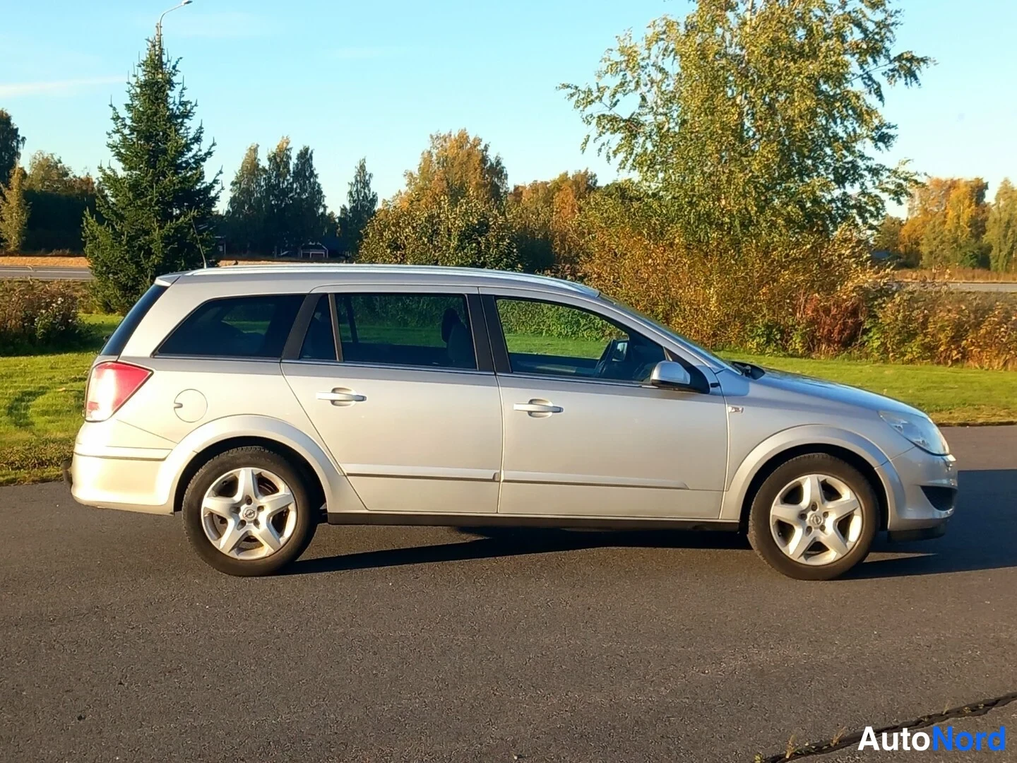 Sivulta: Silver Opel Astra Caravan side profile on asphalt with trees