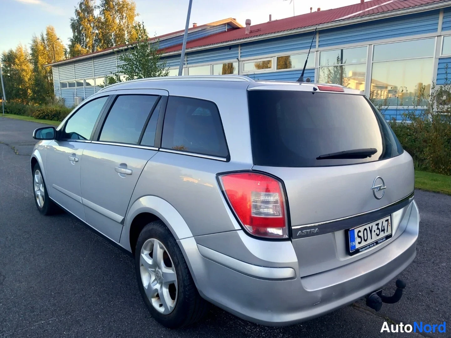 Takaviisto: Hopeanvärinen Opel Astra -farmari takaa vasemmasta kolmannesta kuvakulmasta, takavalo ja rekisterikilpi näkyvissä.