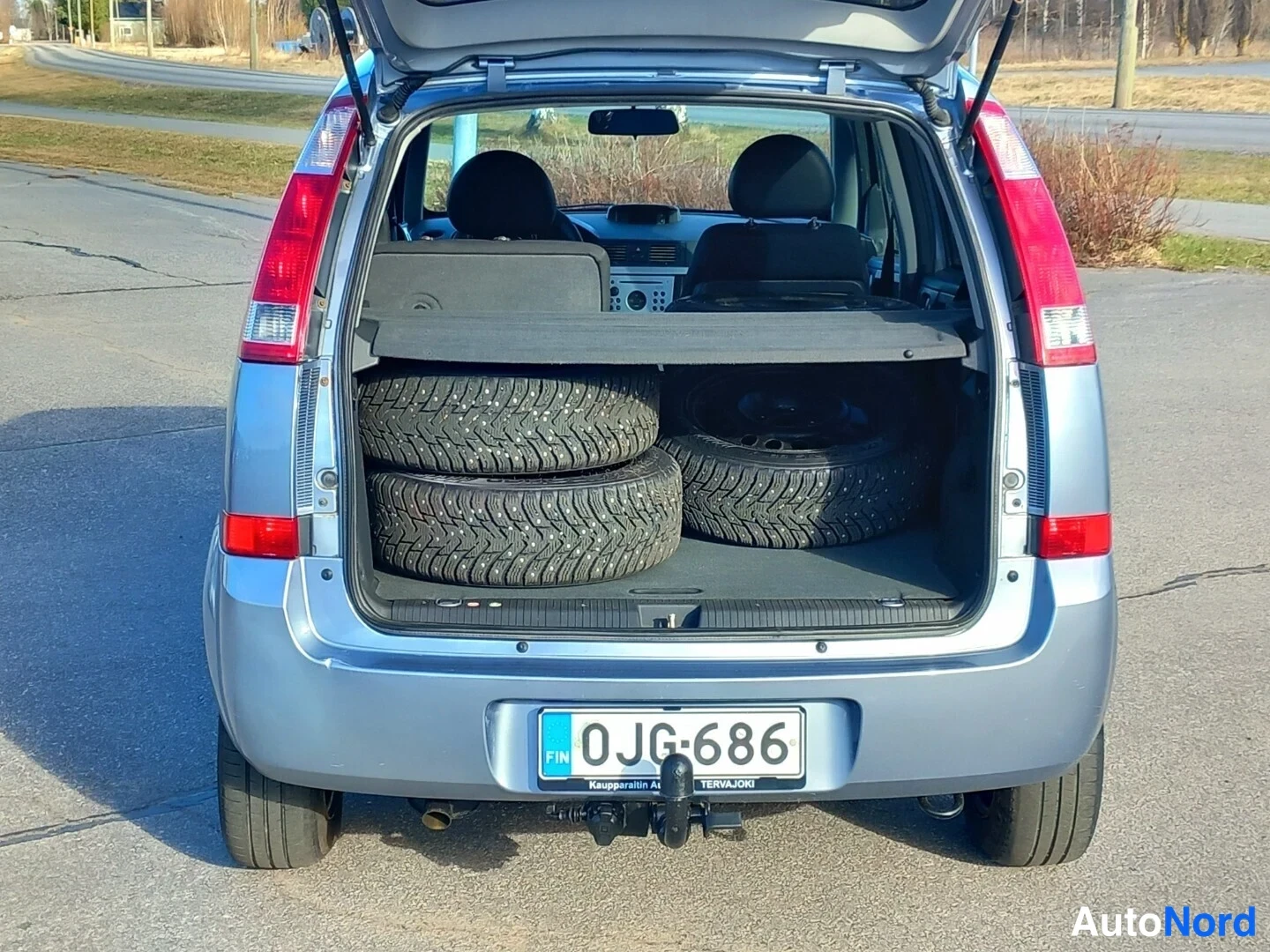 Takaa: Auton takaosa, avattu takaluukku ja niitattuja talvirenkaita tavaratilassa, rekisterikilpi.