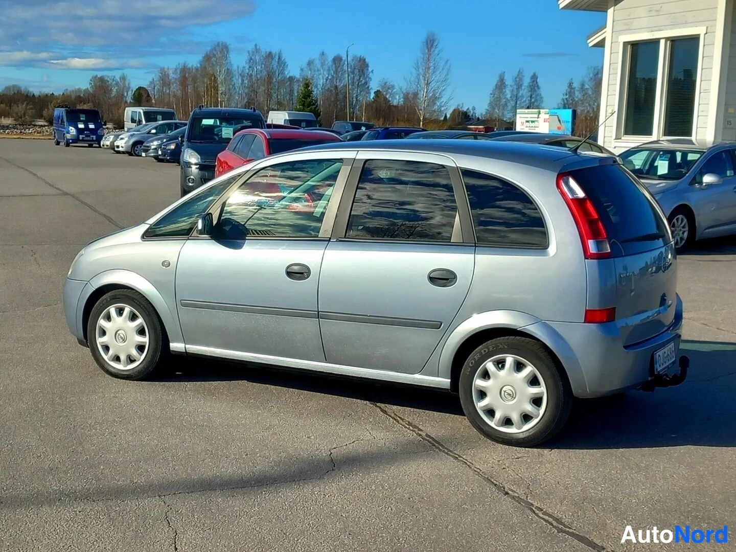 Takaviisto: Opel Meriva -auton takakulmakuva vasemmalta, takavalot ja kylki näkyvissä, hopeinen koriväri.
