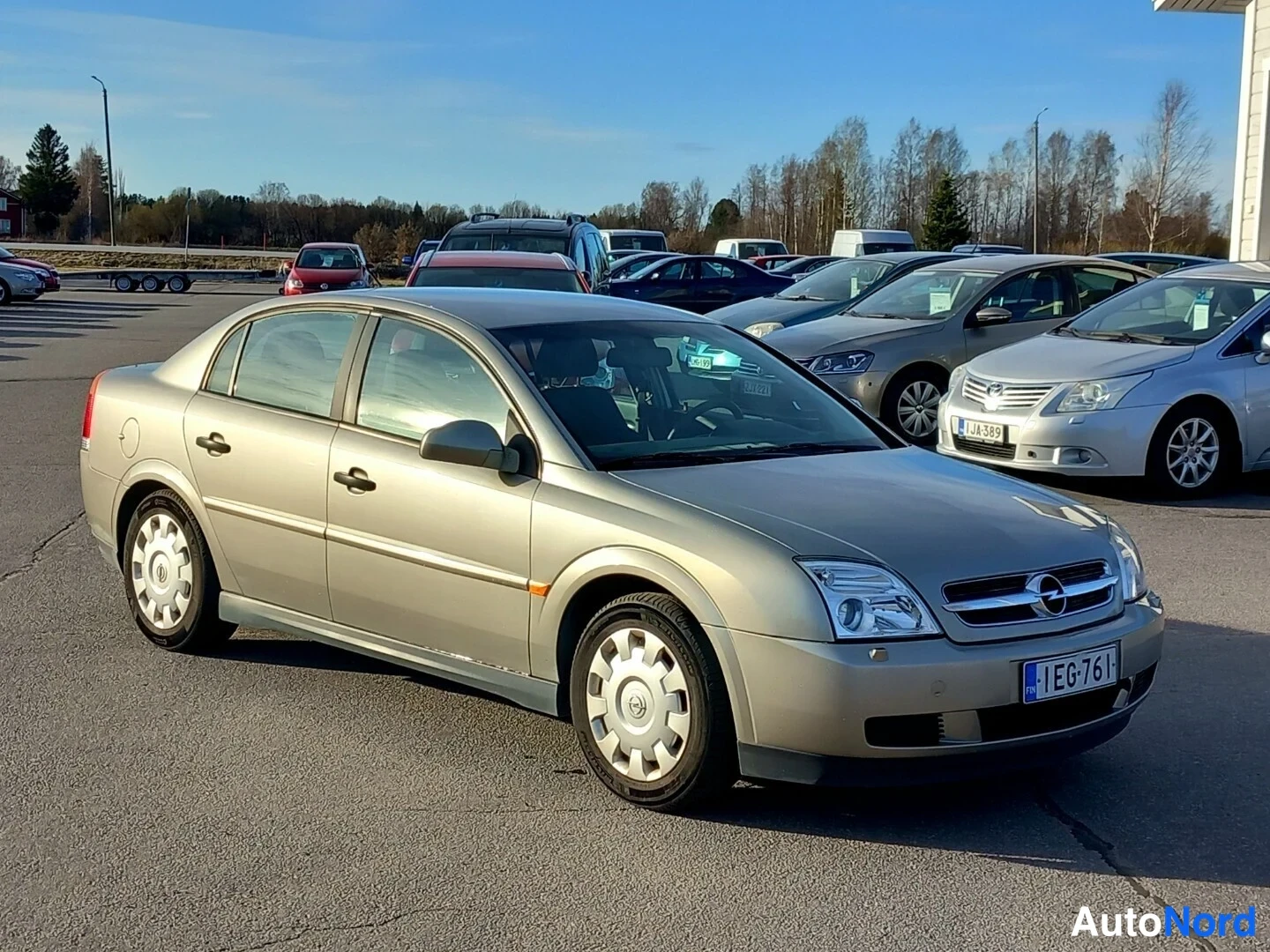 Etuviisto, nokka oikealle: Beige sedan etuviistossa parkkialueella muiden autojen edessä, rekisterikilpi EG-761.