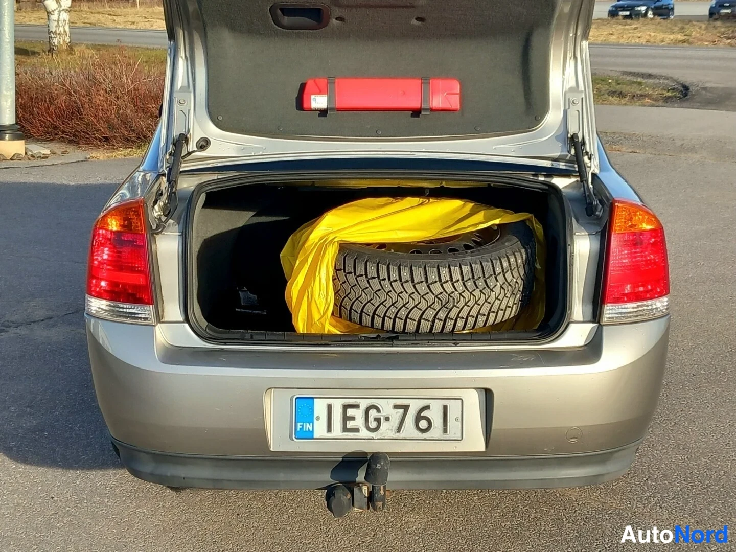 Takaa: Opel Vectran takaluukku auki, renkaita ja keltainen suojakangas tavaratilassa, kilpi