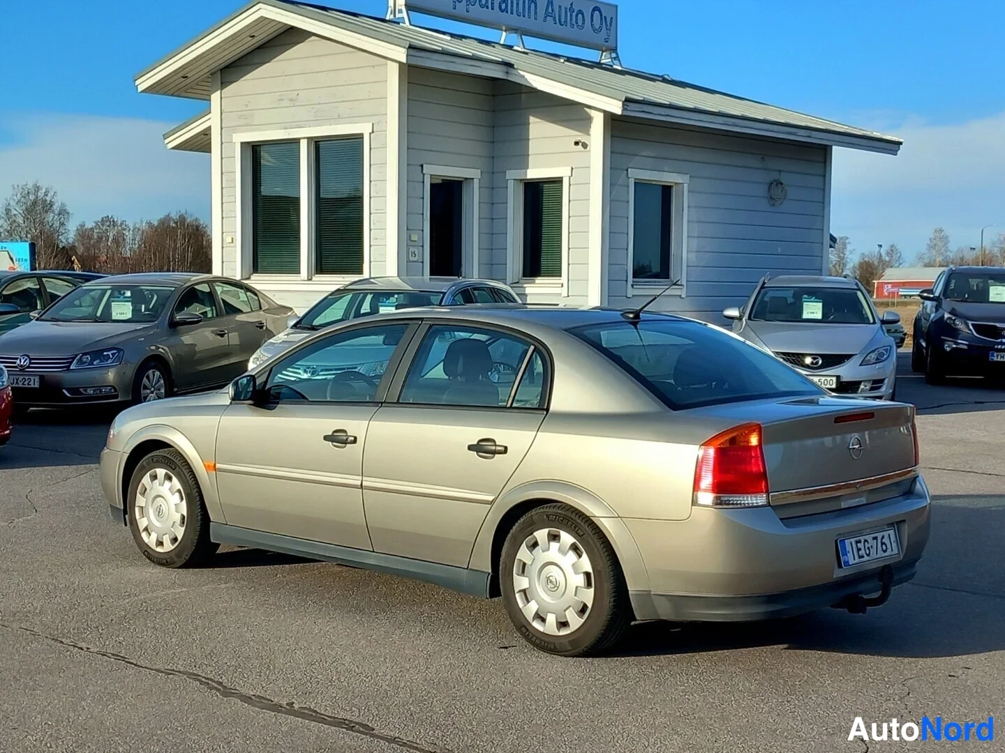 Takaviisto: Beige sedan takaviistossa autoliikkeen pihalla, rekisterikilpi EG-761.