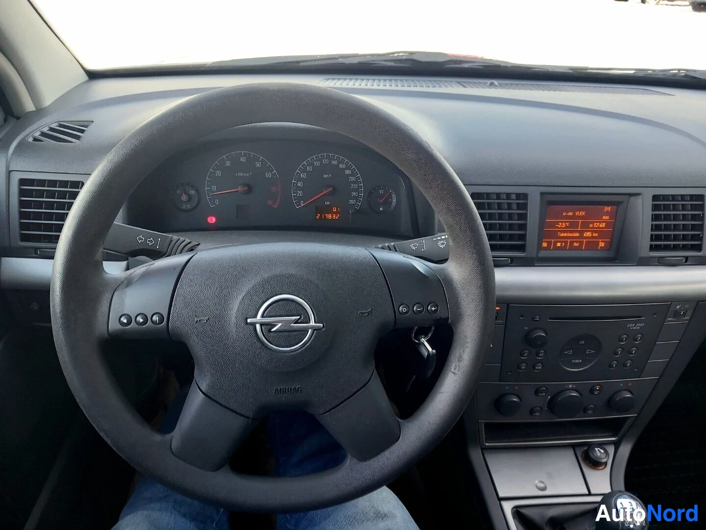 Muu: Ohjaamosta kuva Opel-ohjauspyörästä, mittaristosta ja keskikonsolista. Mittariston näytössä lukema 211932 km.