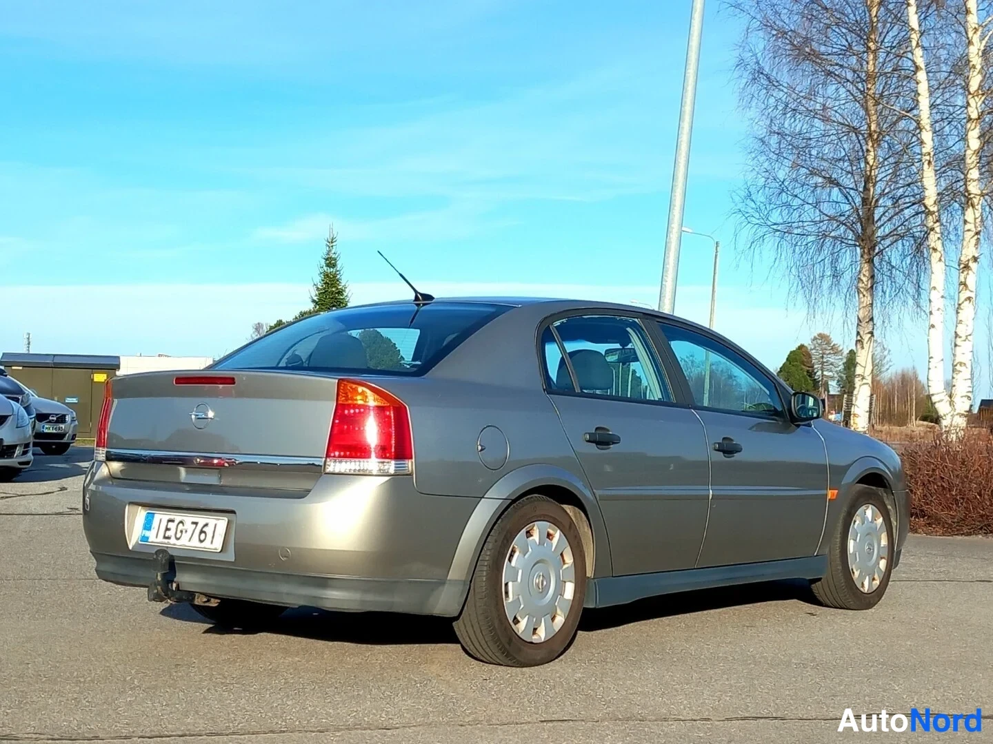 Takaviisto: Beige sedan takaviistossa auringossa, rekisterikilpi EG-761 ja vetokoukun pallo takapuskurin alla.
