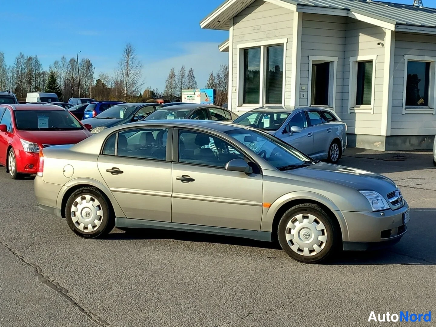 Etuviisto, nokka oikealle: Beige Opel Vectra -sedan etukulmasta oikealle päin parkkihallon edessä.