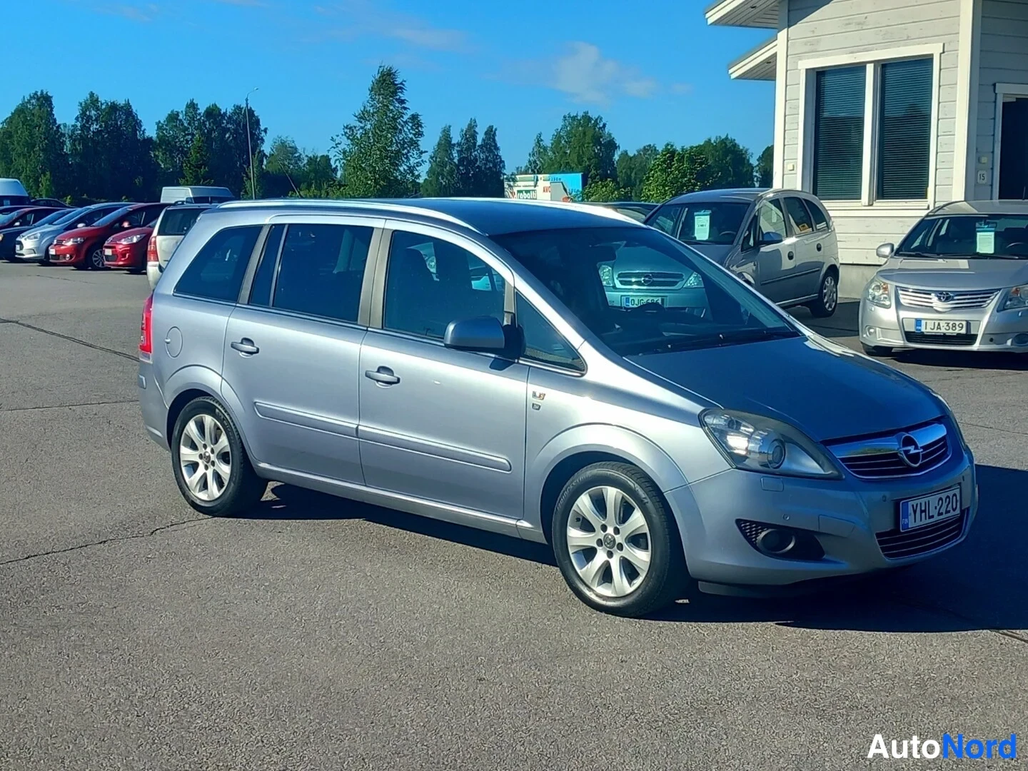 Etuviisto, nokka oikealle: Hopeanharmaa Opel Zafira -pakettiauto kolmannelta kulmalta edestä oikealta, rekisteritunnus.