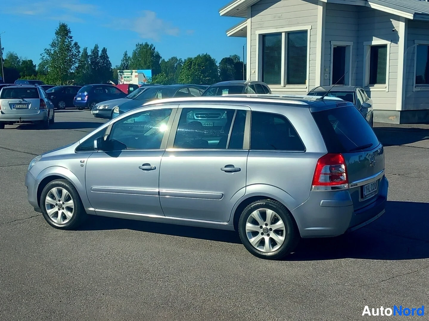 Takaviisto: Hopeanharmaa tila-auto takaa vasemmalta kuvattuna paikoitusalueella.