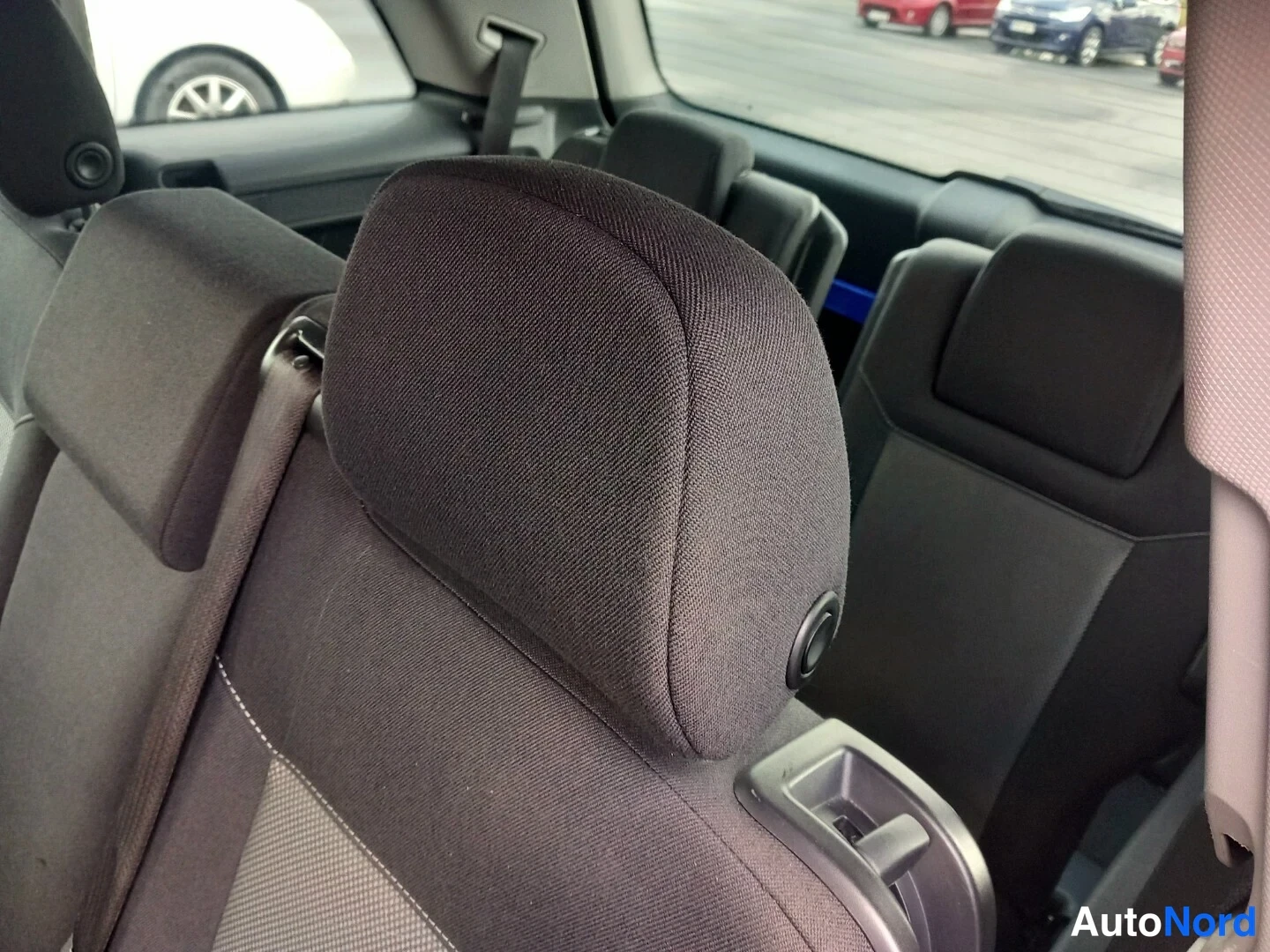 Takaistuimet: Close-up view of the backrest and headrest of a rear seat upholstered in dark gray fabric. A three-point seatbelt is visible running along the side of the seat.
