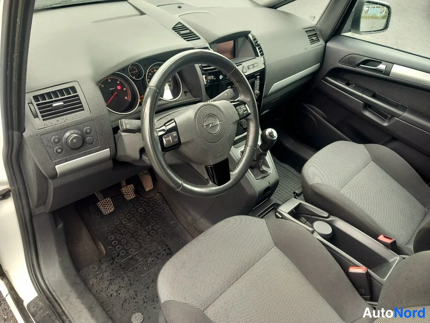 Muu: Ohjaamon näkymä kuljettajan puolelta: Opel-merkkinen ohjauspyörä, mittarit, manuaalivaihtajan vapaa ja tekstiilietuistuimet; kuva on sama kuin edellinen kuva.