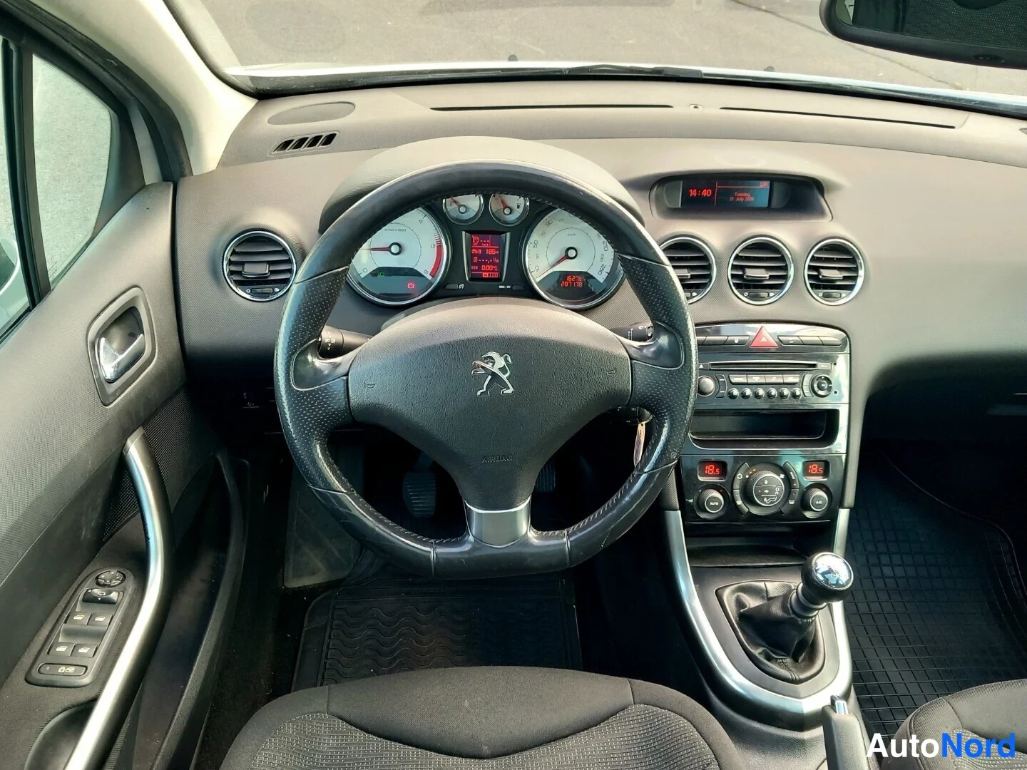 Muu: Ohjauspyörä Peugeot-logolla ja mittaristo, jonka näyttö näyttää '14:40' ja '18.5'; radiopaneeli, ilmastointipainikkeet ja manuaalivaihteen vipu näkyvät myös.
