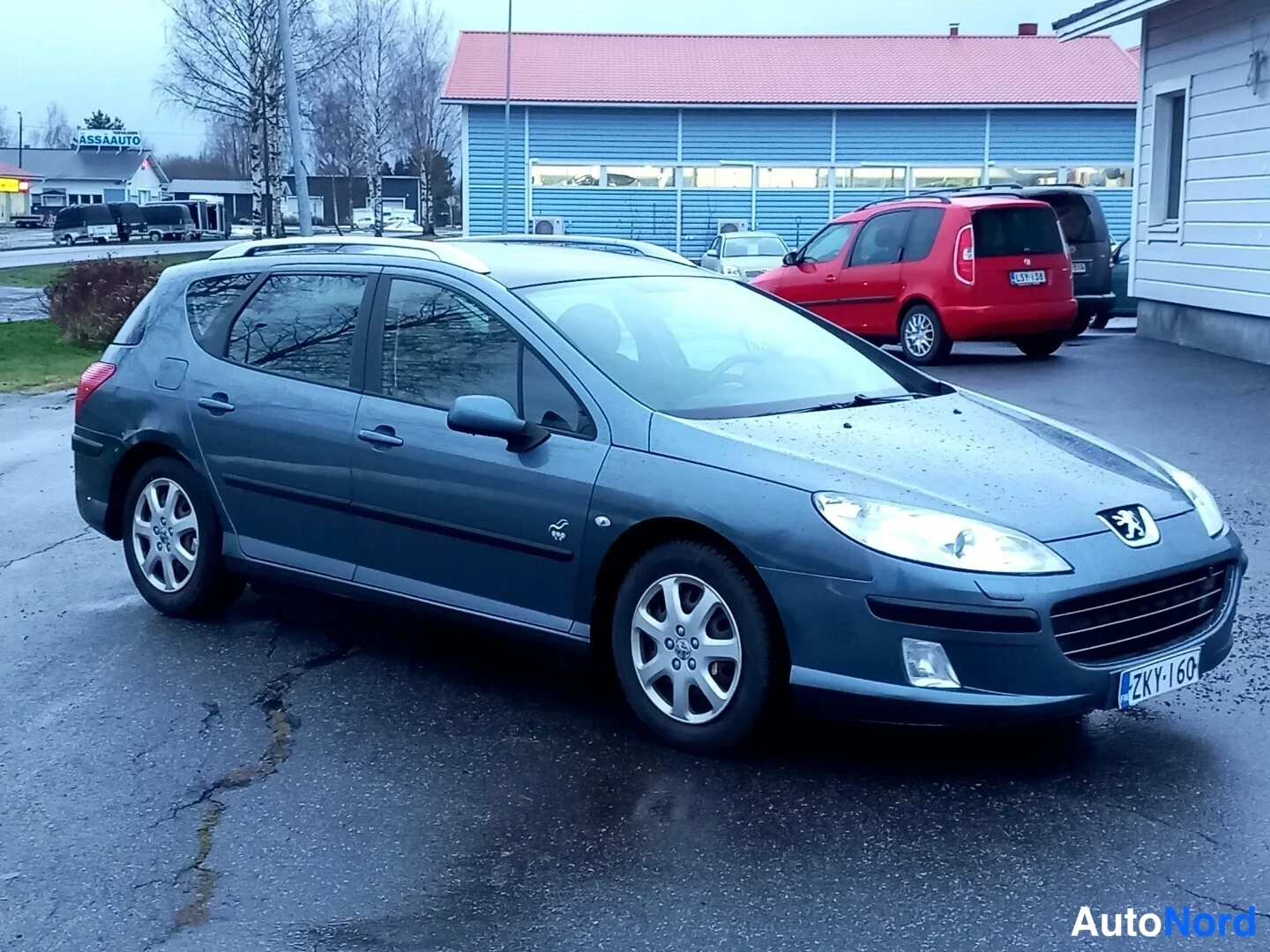 Etuviisto, nokka oikealle: Sinisenharmaa Peugeot 407 -farmari kulmassa edestä oikealta, kylki ja keulalle näkyvät pihalla.