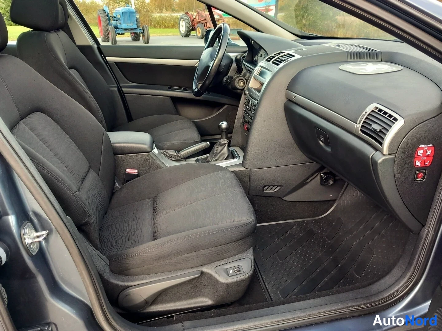 Muu: Peugeot 407 -matkailuauton sisätilat vasemmalta: tummat kankaat etuistuimet, manuaali vaihteenvaihtaja, tumma kojelauta ja ovenavaus vasemmalla.