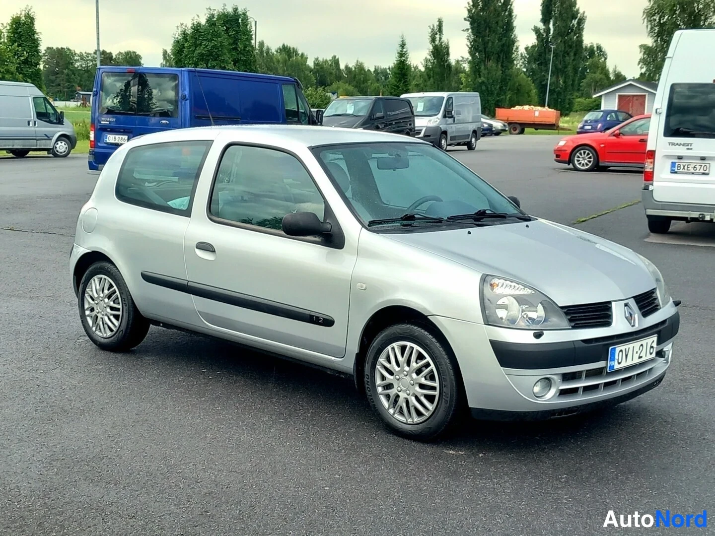 Etuviisto, nokka oikealle: Hopeanharmaa kolmiovinen Renault Clio -henkilöauto parkkipaikalla, kolmen neljäsosan etukuva keula oikealla.