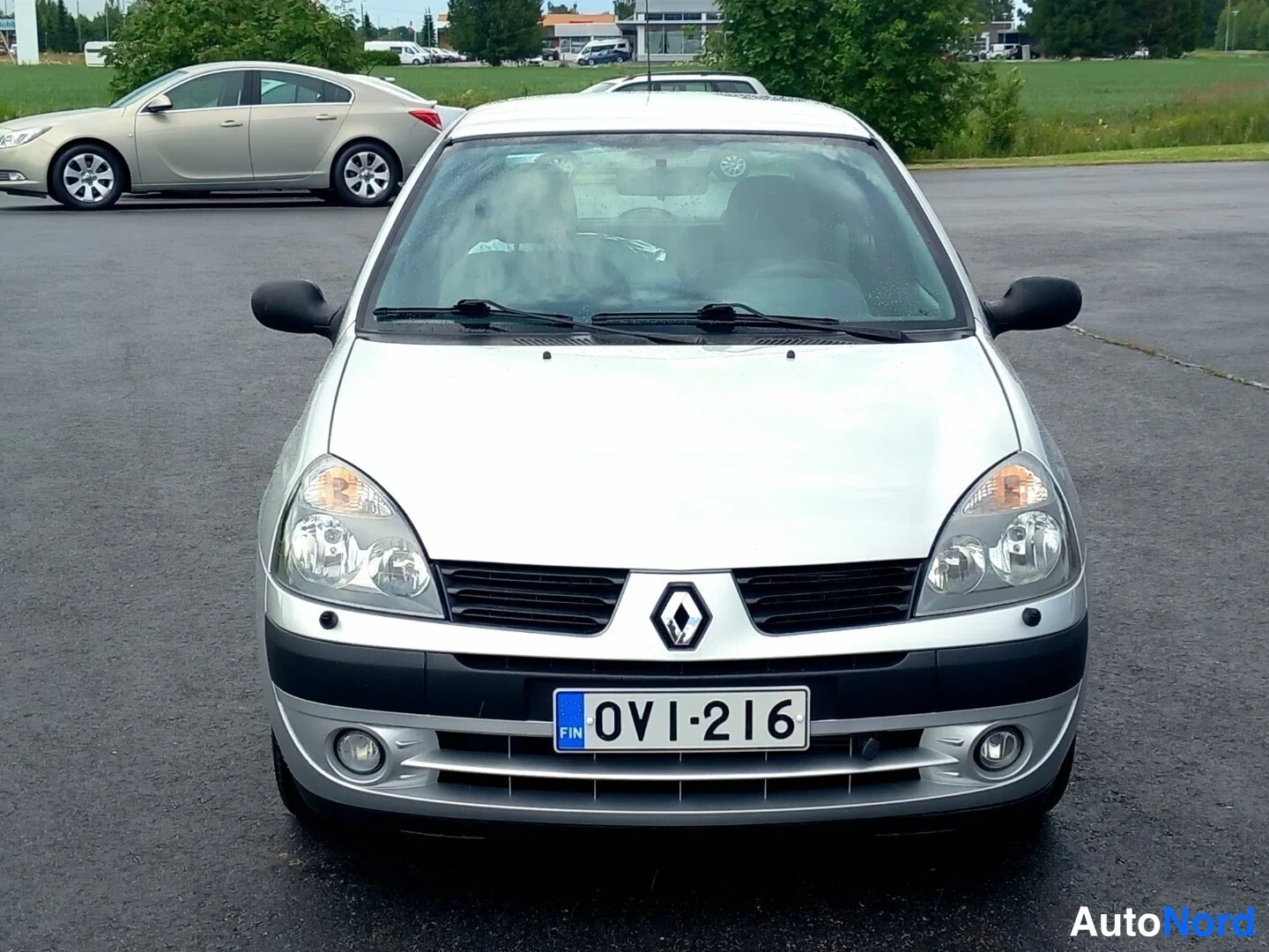 Edestä: Auton etusiluetti: hopeanharmaa Renault Clio, etumoottoritila ja ajovalot näkyvät, rekisterikilpi 0VI-216