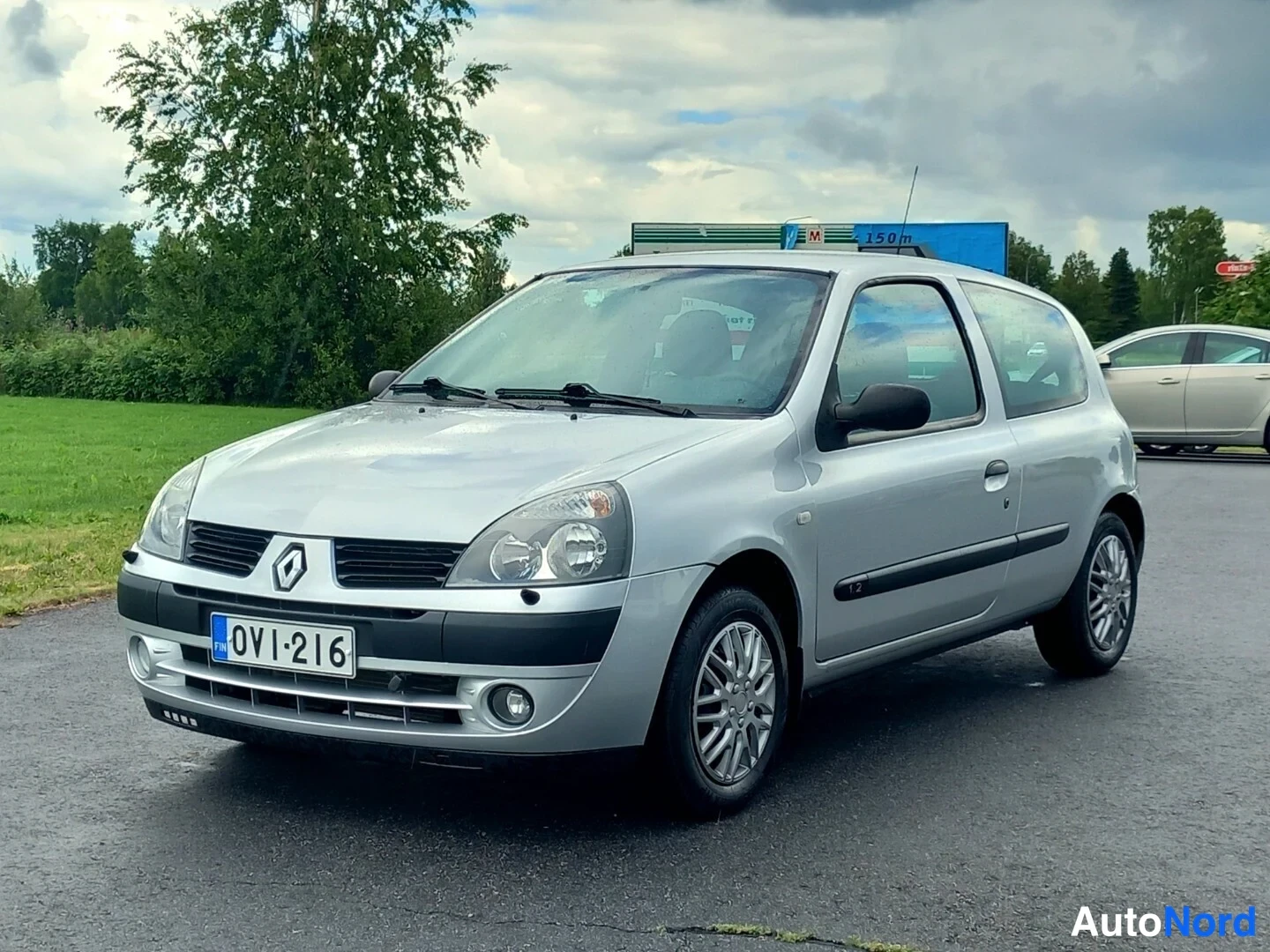 Etuviisto, nokka vasemmalle: Hopeanvärinen Renault Clio -henkilöauto edestä kolmanneltaa kuvakulmalta, rekisterikilpi.