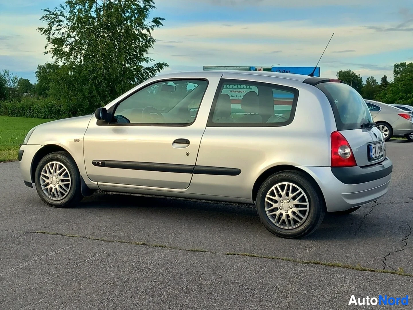 Takaviisto: Hopeinen Renault Clio -henkilöauto kolmesta neljäsosasta takaa vasemmalta kuvattuna parkkipaikalla.