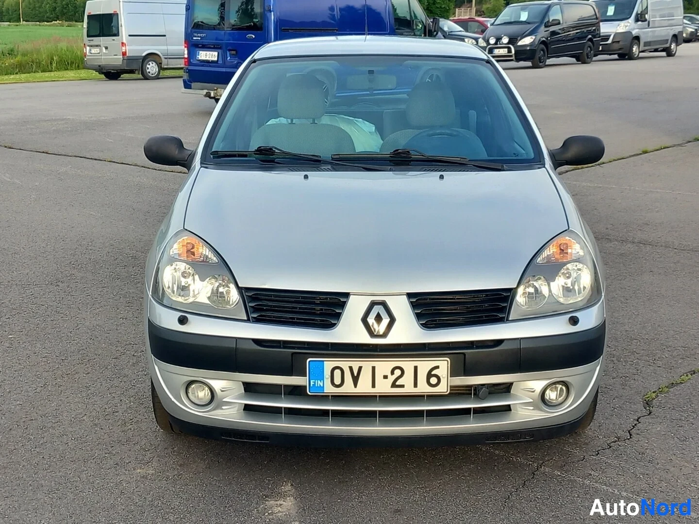 Edestä: Hopeisen Renault Clion etunäkymä, rekisterikilpi, auton edessä parkkialueella.